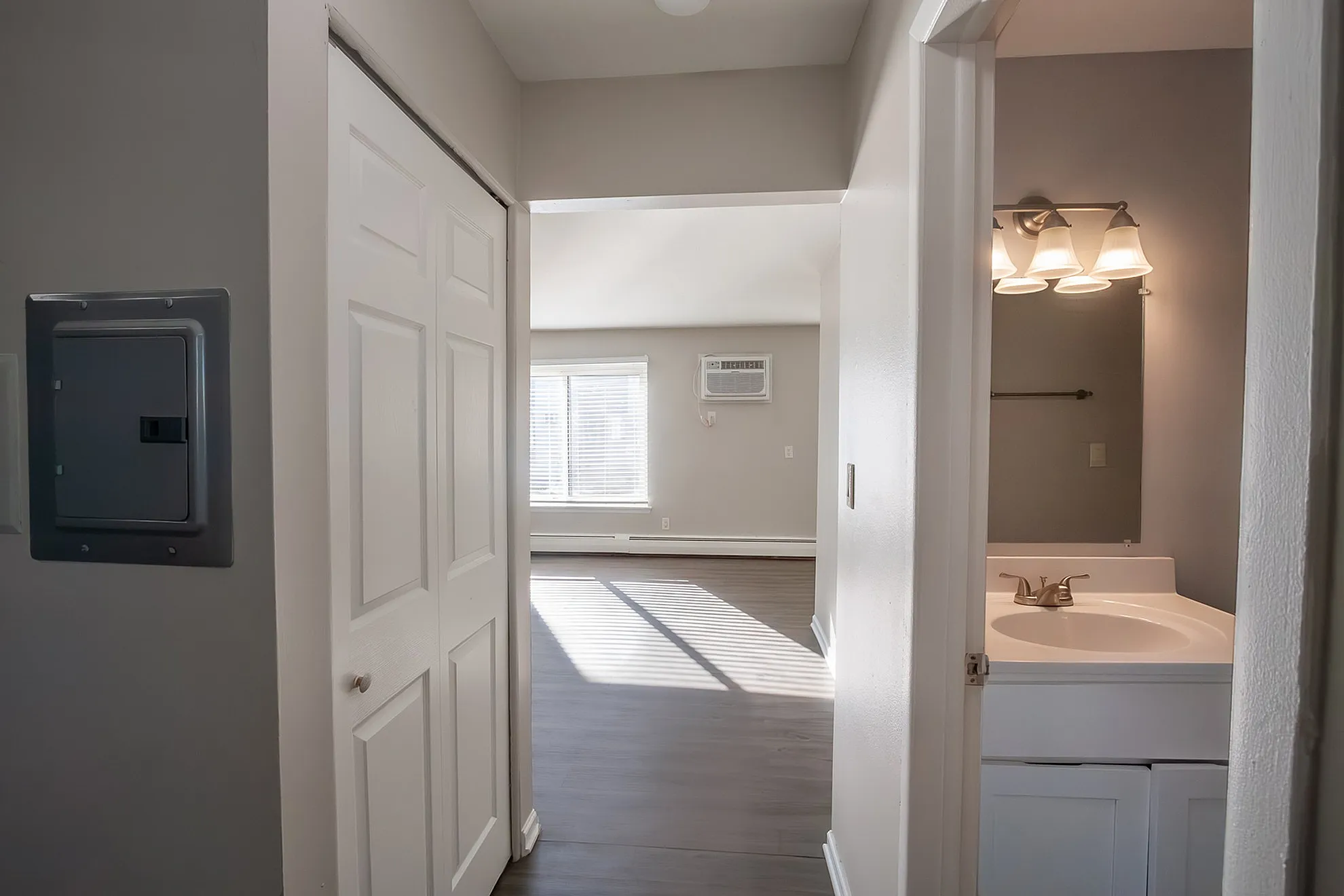 Bright hallway leading to a sunlit living area with modern flooring and a cozy bathroom space on the side.