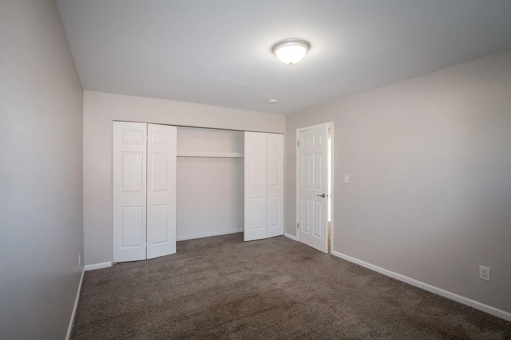 Bright, neutral-toned bedroom with plush carpet and spacious closet, offering a cozy and inviting atmosphere.