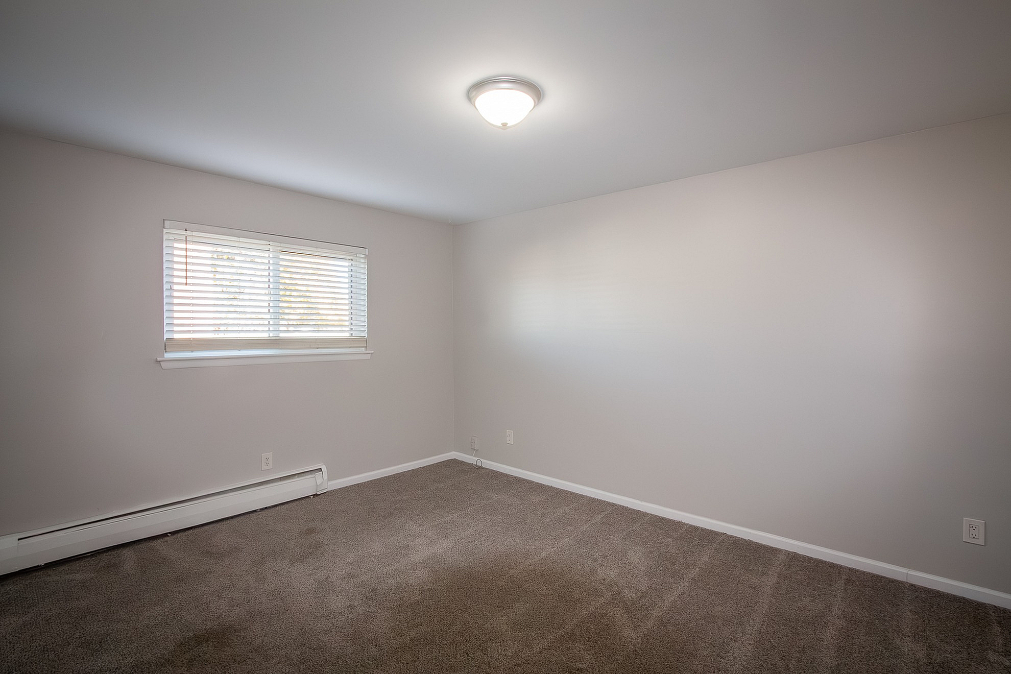 Bright and inviting room with soft carpeting, natural light from large window, and modern light fixture; perfect for a cozy retreat.