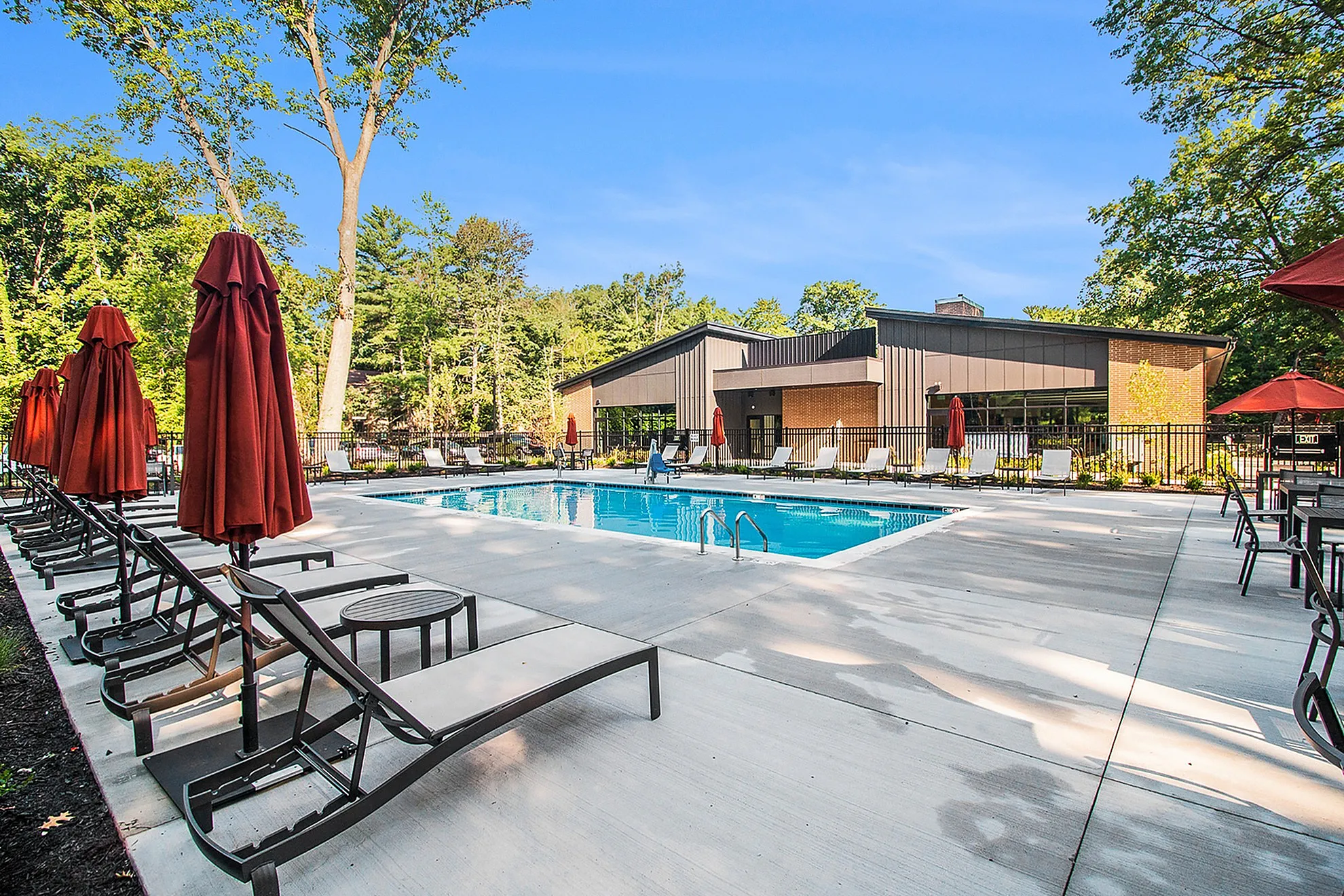 Inviting outdoor pool area with stylish lounge chairs and vibrant red umbrellas, surrounded by lush greenery and modern architecture.