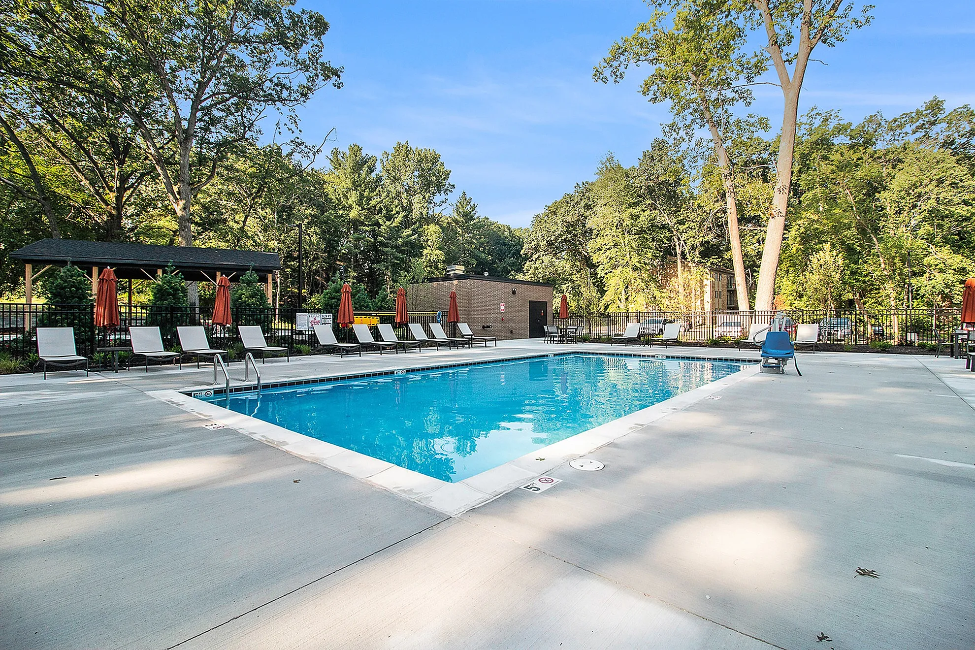Inviting outdoor pool area surrounded by lush trees, featuring comfortable lounge chairs and shaded seating for relaxation.