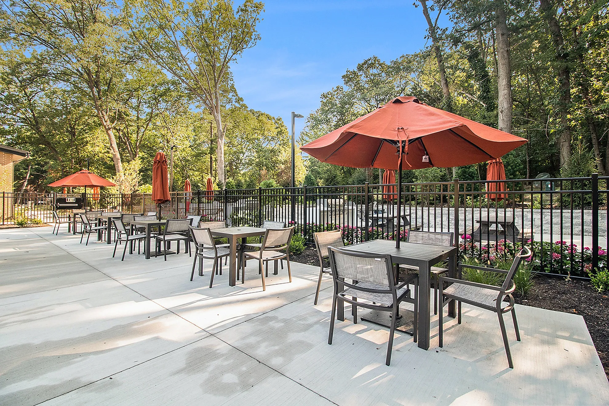 Inviting patio area with modern outdoor furniture and stylish orange umbrellas, surrounded by lush greenery, perfect for relaxation and alfresco dining.
