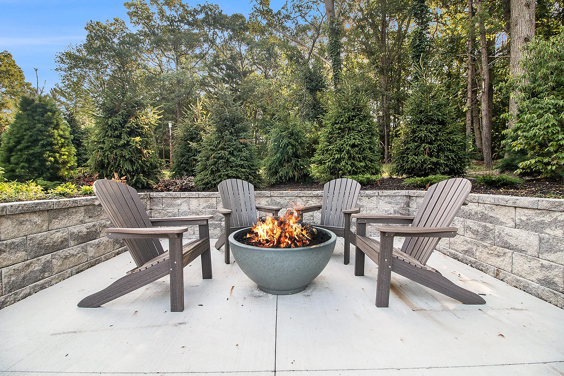 Inviting outdoor patio featuring a cozy fire pit surrounded by four Adirondack chairs, perfect for relaxing amidst lush greenery.
