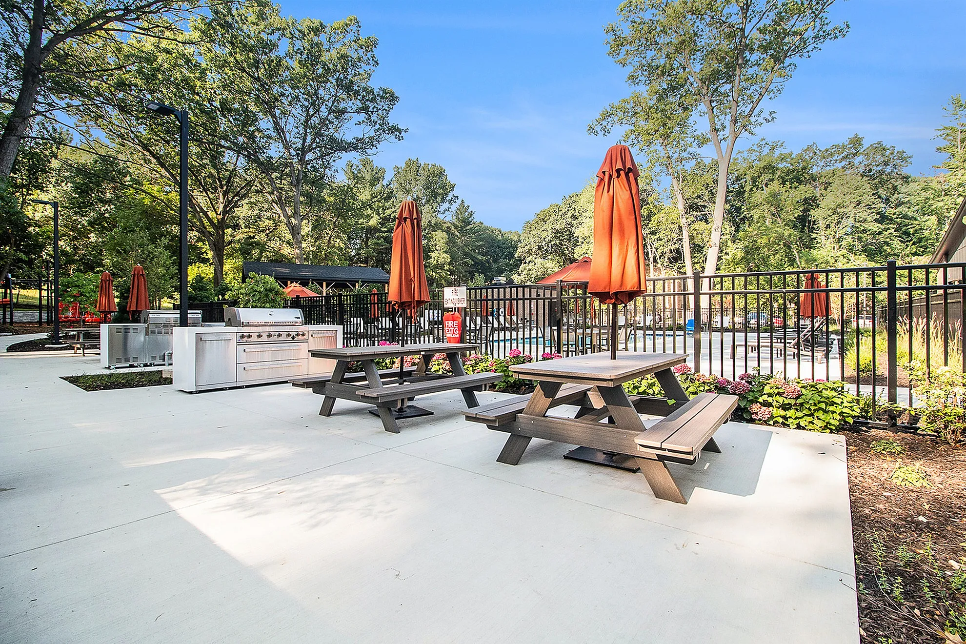 Inviting outdoor BBQ area with modern grill, picnic tables, and vibrant umbrellas, set amidst lush greenery and serene surroundings.