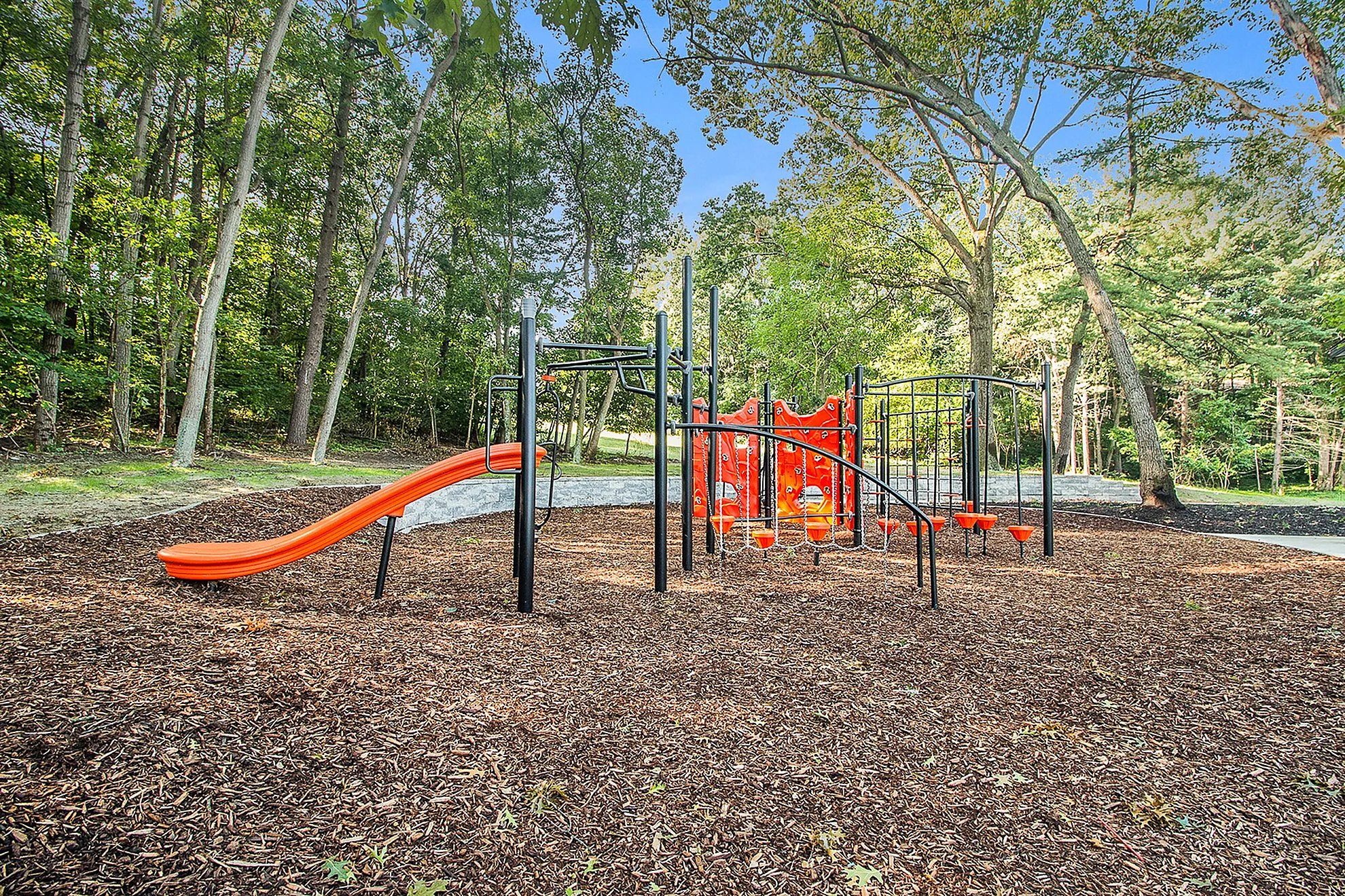 Inviting playground featuring vibrant orange slides and climbing structures, nestled in a lush wooded area.