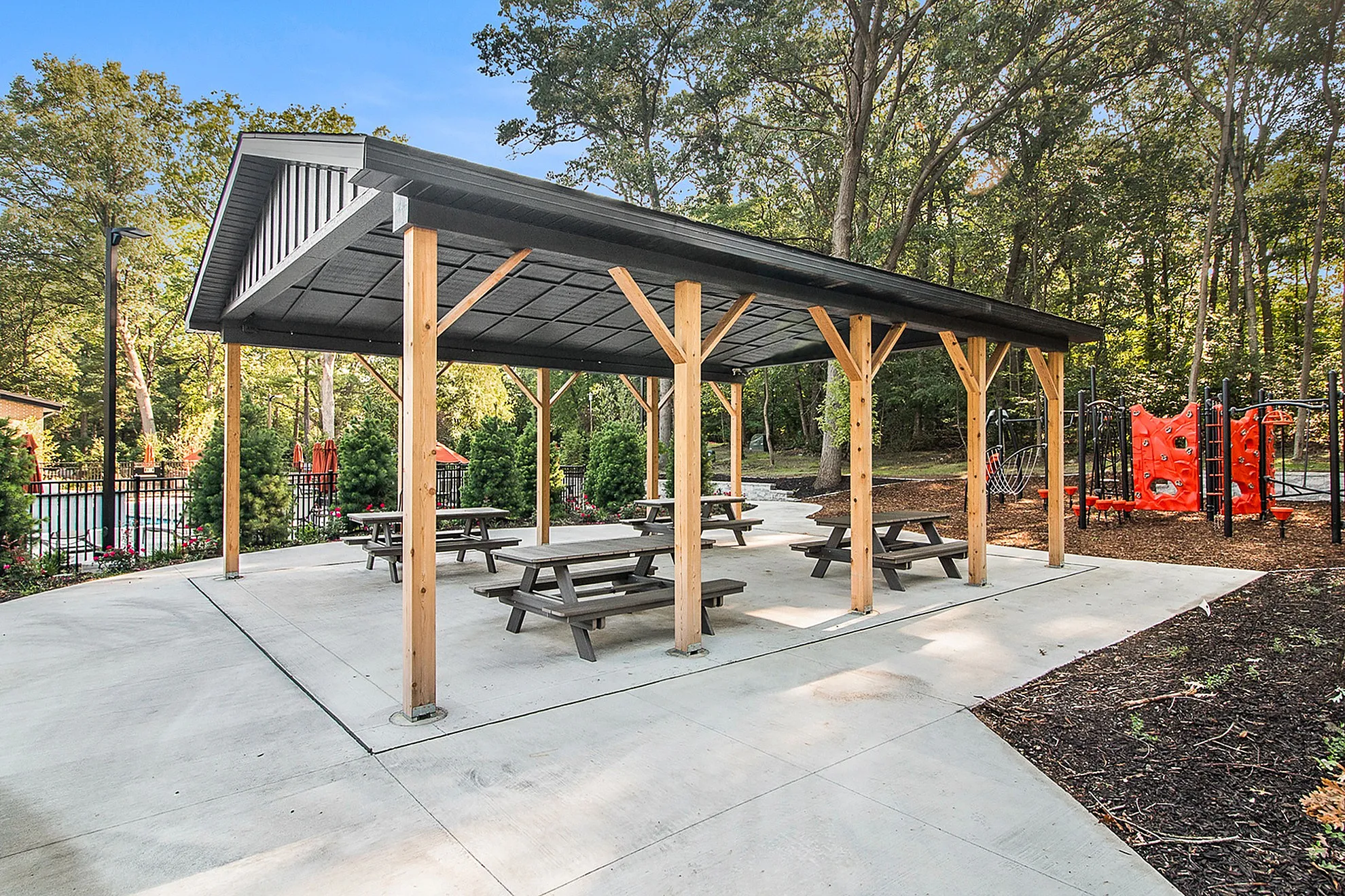 Charming outdoor pavilion with picnic tables and a vibrant playground, nestled in a lush green setting.