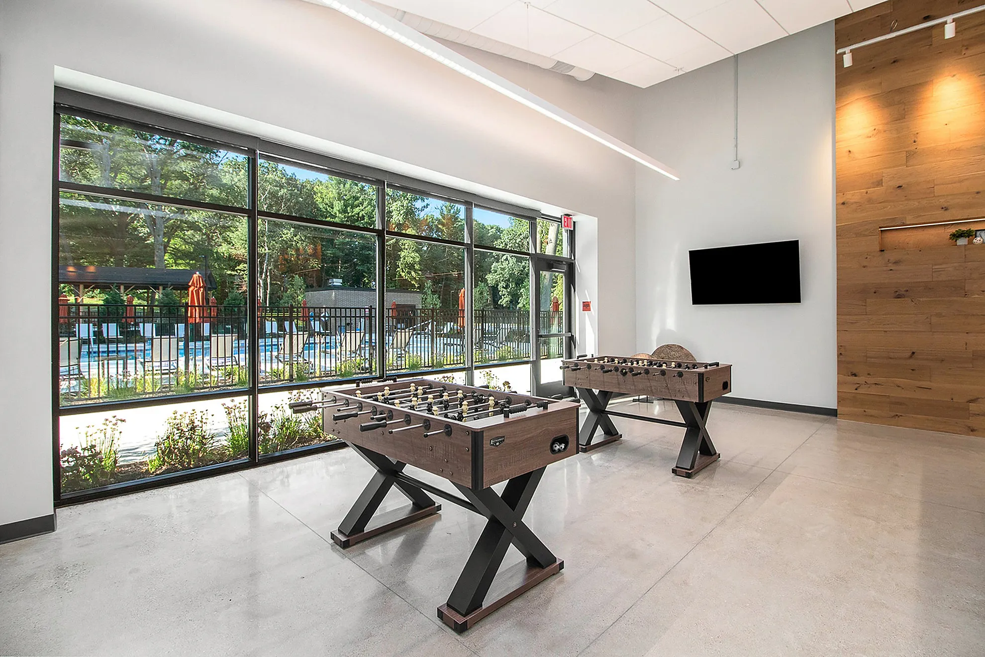 Bright recreational room with foosball tables and large windows overlooking a serene pool area.