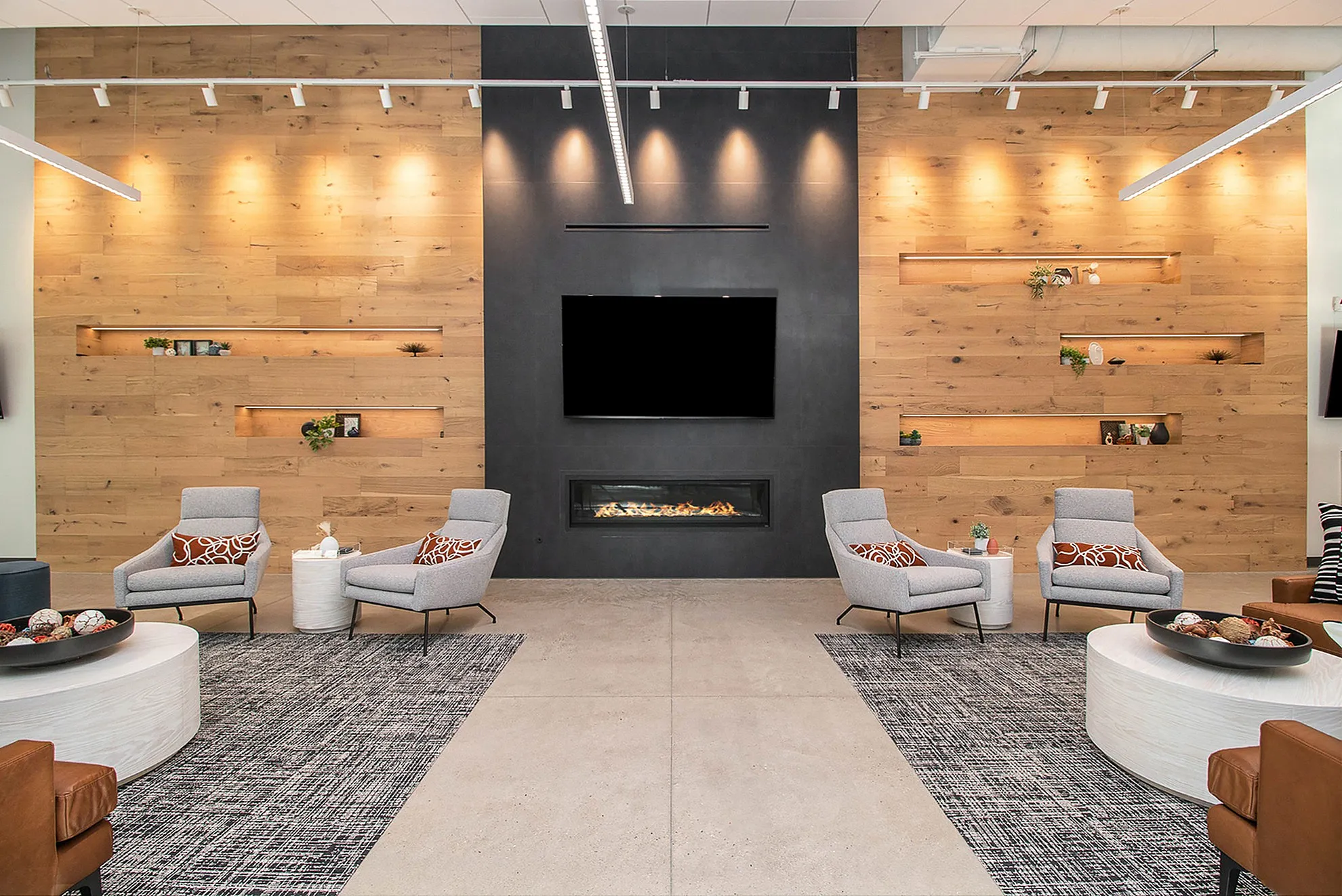 Modern lounge area with stylish gray chairs, wood-accented walls, integrated fireplace, and artful shelving.