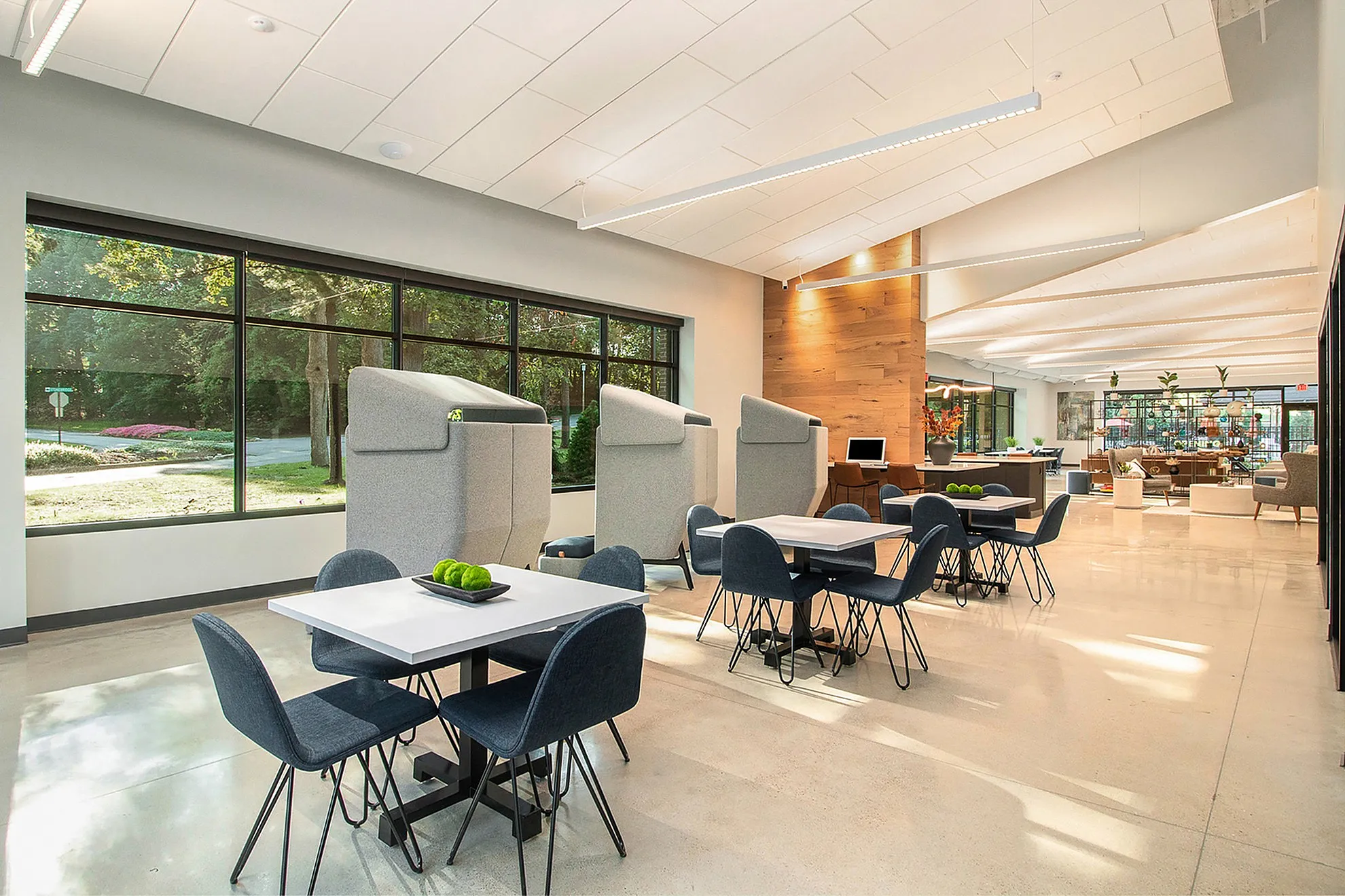 Bright and modern communal space with sleek tables and chairs, large windows, and stylish wooden accents, perfect for social gatherings or co-working.