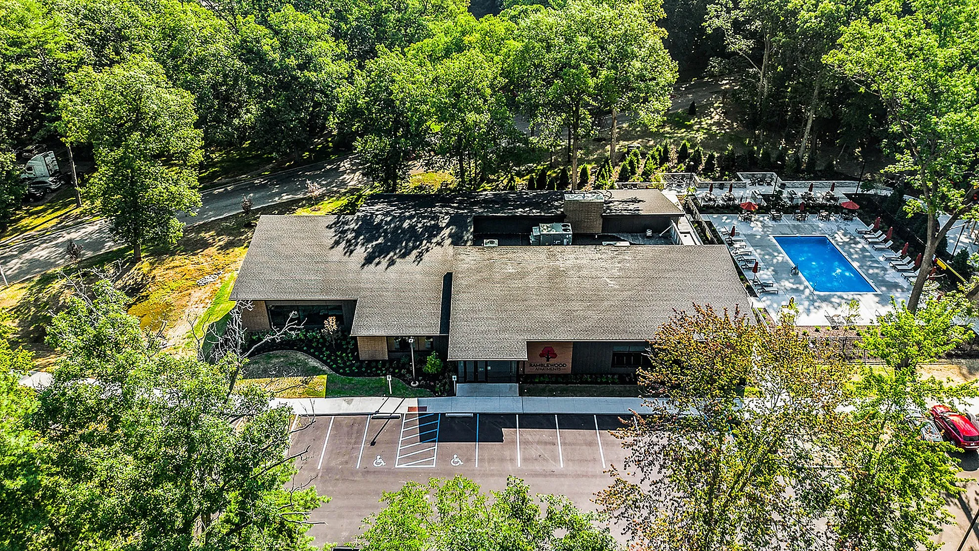 Aerial view of a modern apartment complex surrounded by lush greenery with a sparkling outdoor pool and ample parking space.