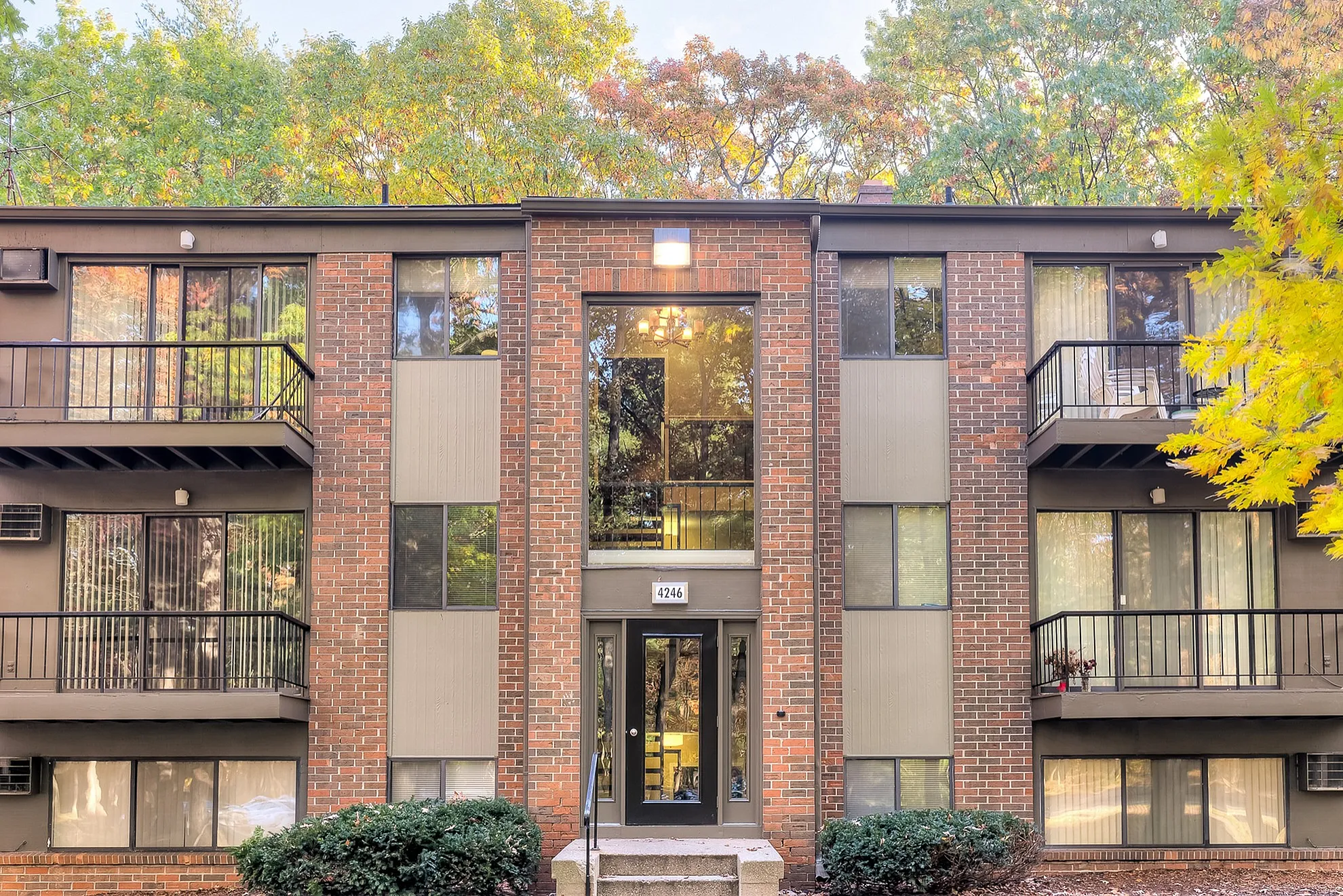 Charming brick apartment building with large windows and private balconies, surrounded by vibrant autumn foliage.
