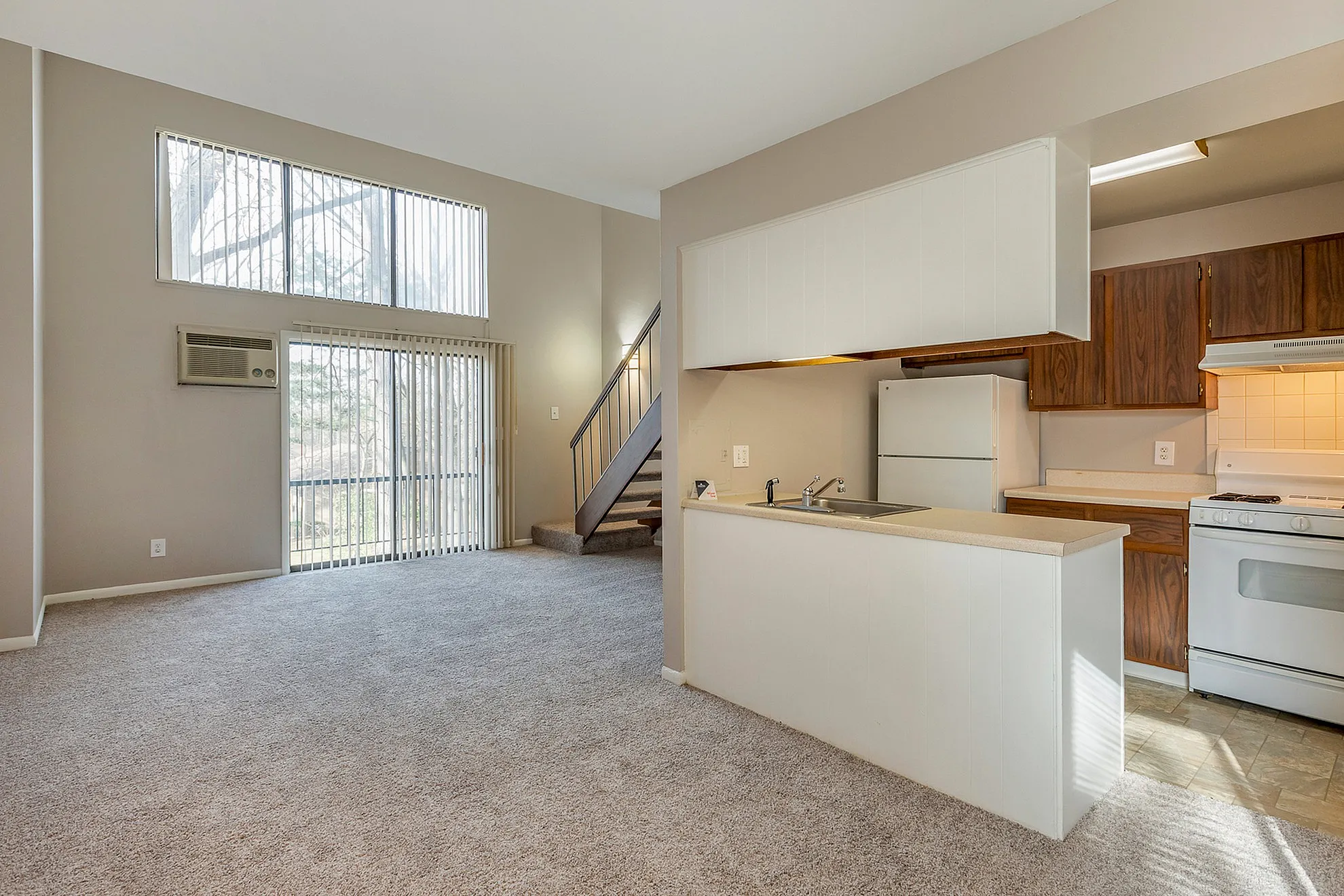 Bright open-plan living area with high ceilings, plush carpet, and a modern kitchen perfect for entertaining.