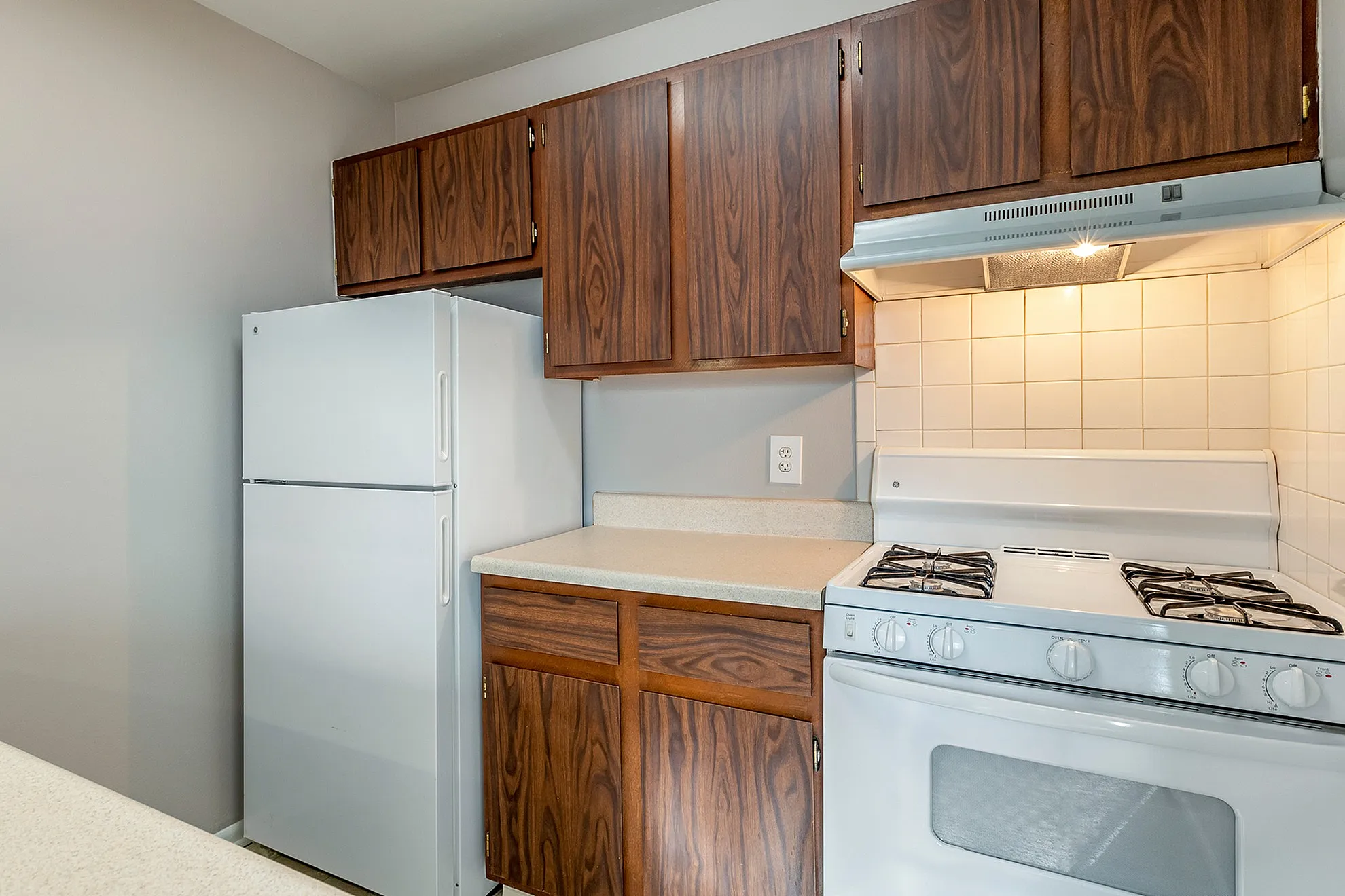 Charming kitchen with elegant wooden cabinets, a sleek white fridge, and a modern gas stove, offering both functionality and style.