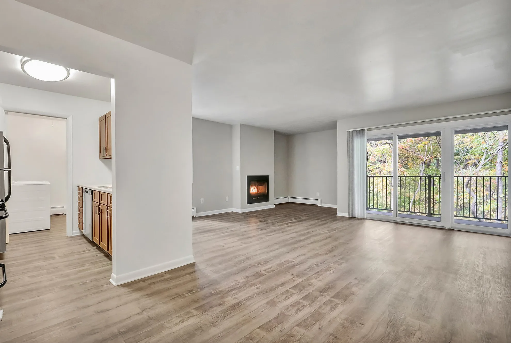 Modern open-concept living room with elegant wood flooring, a cozy fireplace, and tranquil balcony views of lush greenery.