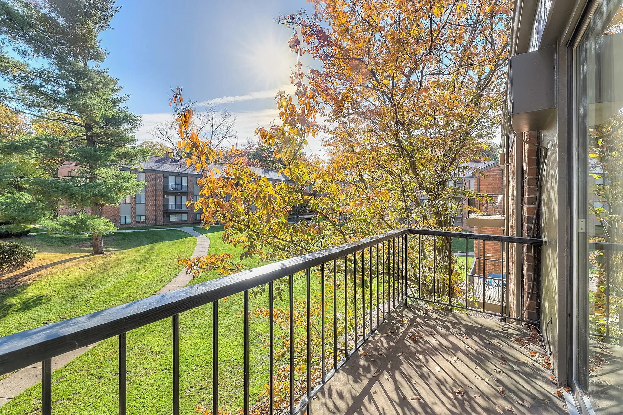 Charming balcony view overlooking a lush green landscape with vibrant autumn foliage under a bright blue sky.