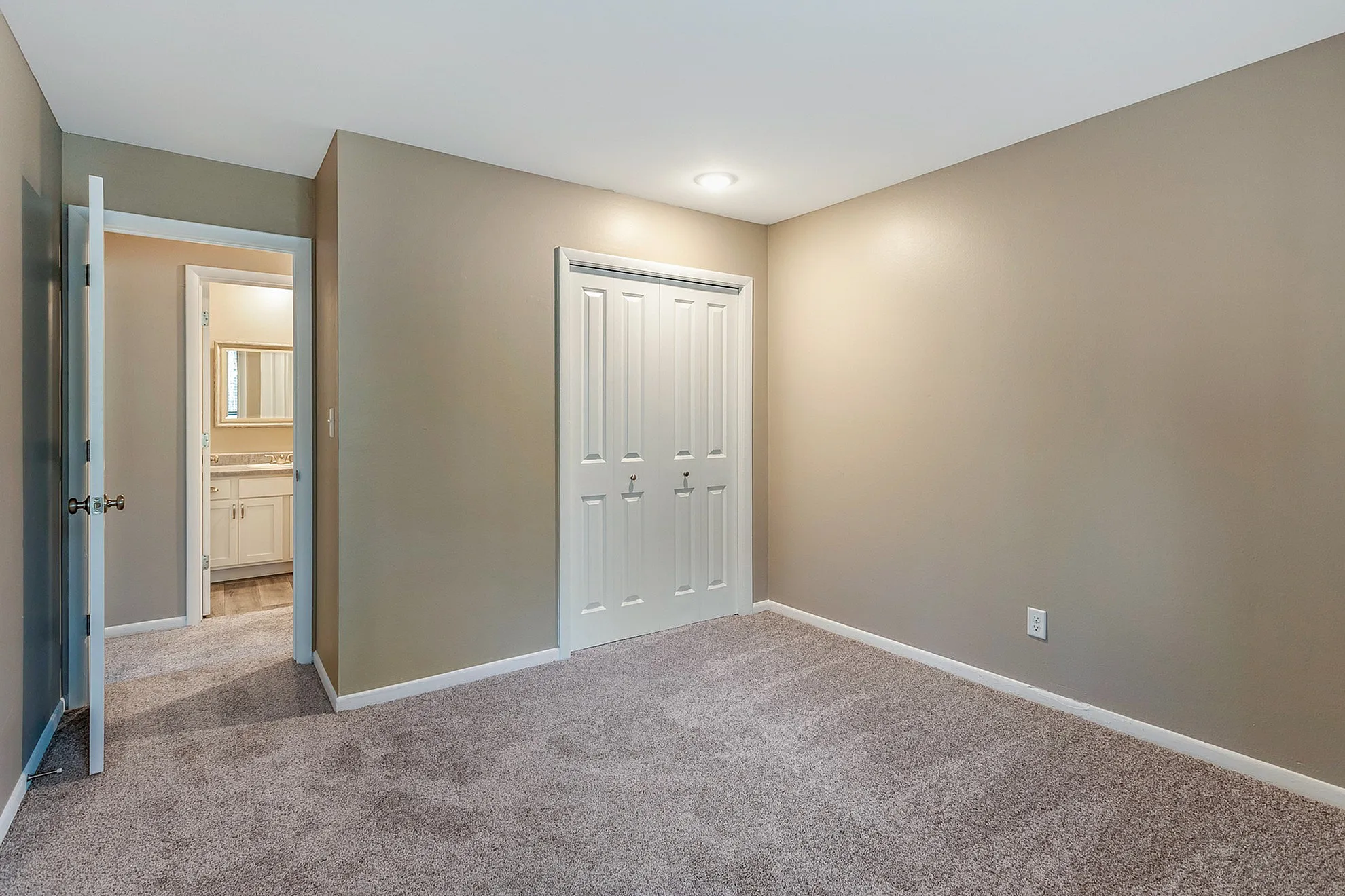 Bright and inviting bedroom featuring soft carpet, neutral walls, and an ensuite bathroom with modern fixtures.