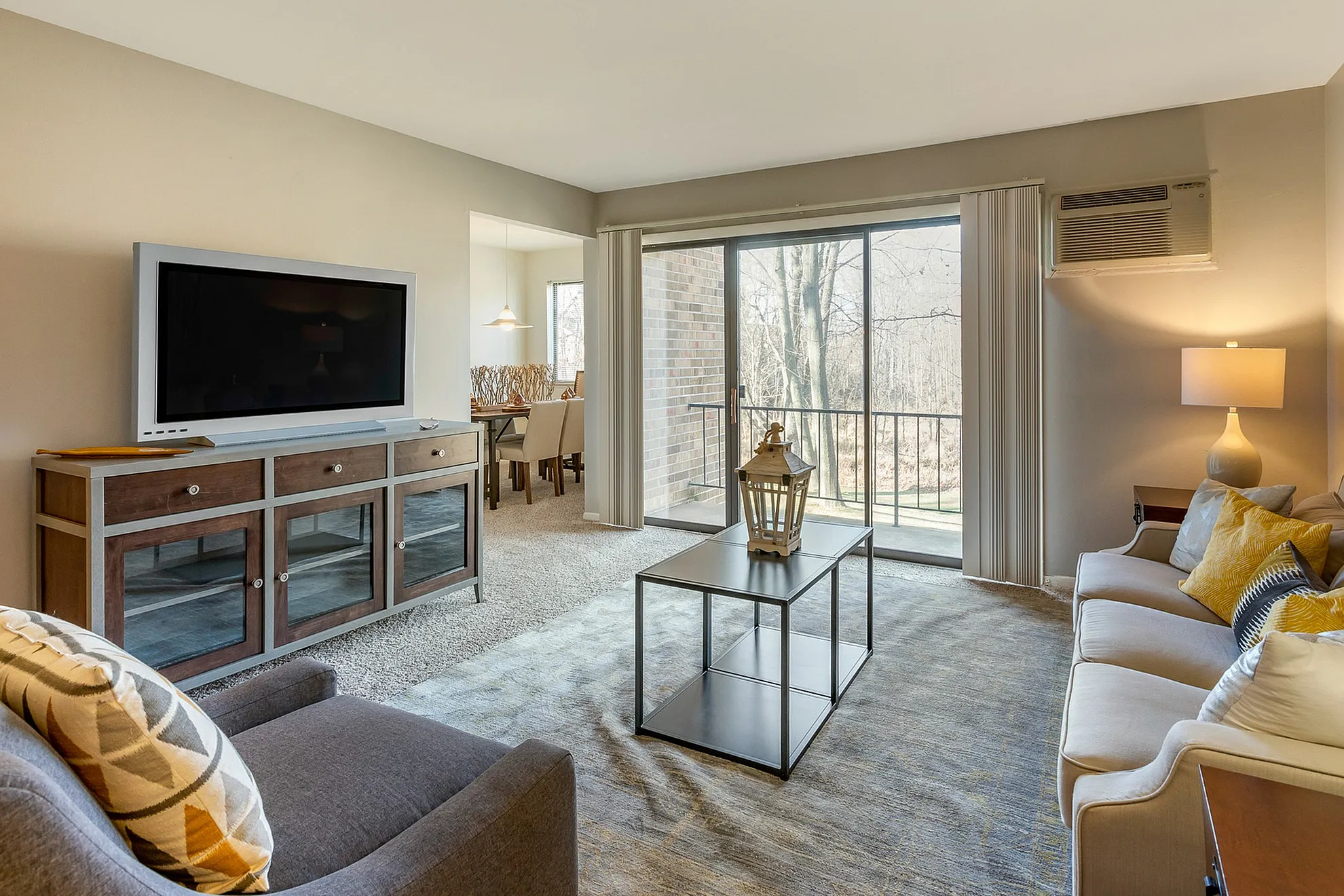 Bright and inviting living room with modern decor, featuring a large flat-screen TV, plush seating, and a sleek coffee table. Sliding glass doors open to a scenic outdoor view, creating a seamless blend of indoor and outdoor living.