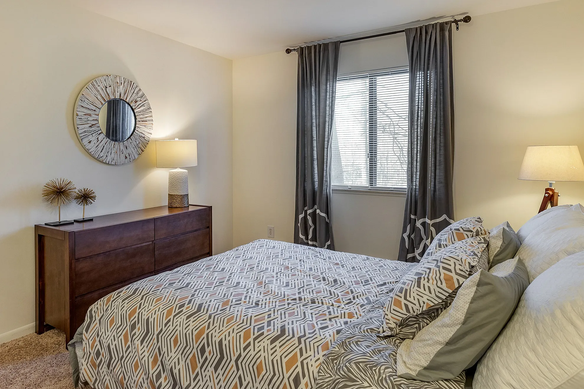 Cozy bedroom with stylish geometric bedding, soft lighting, and a chic wooden dresser with decorative accents.