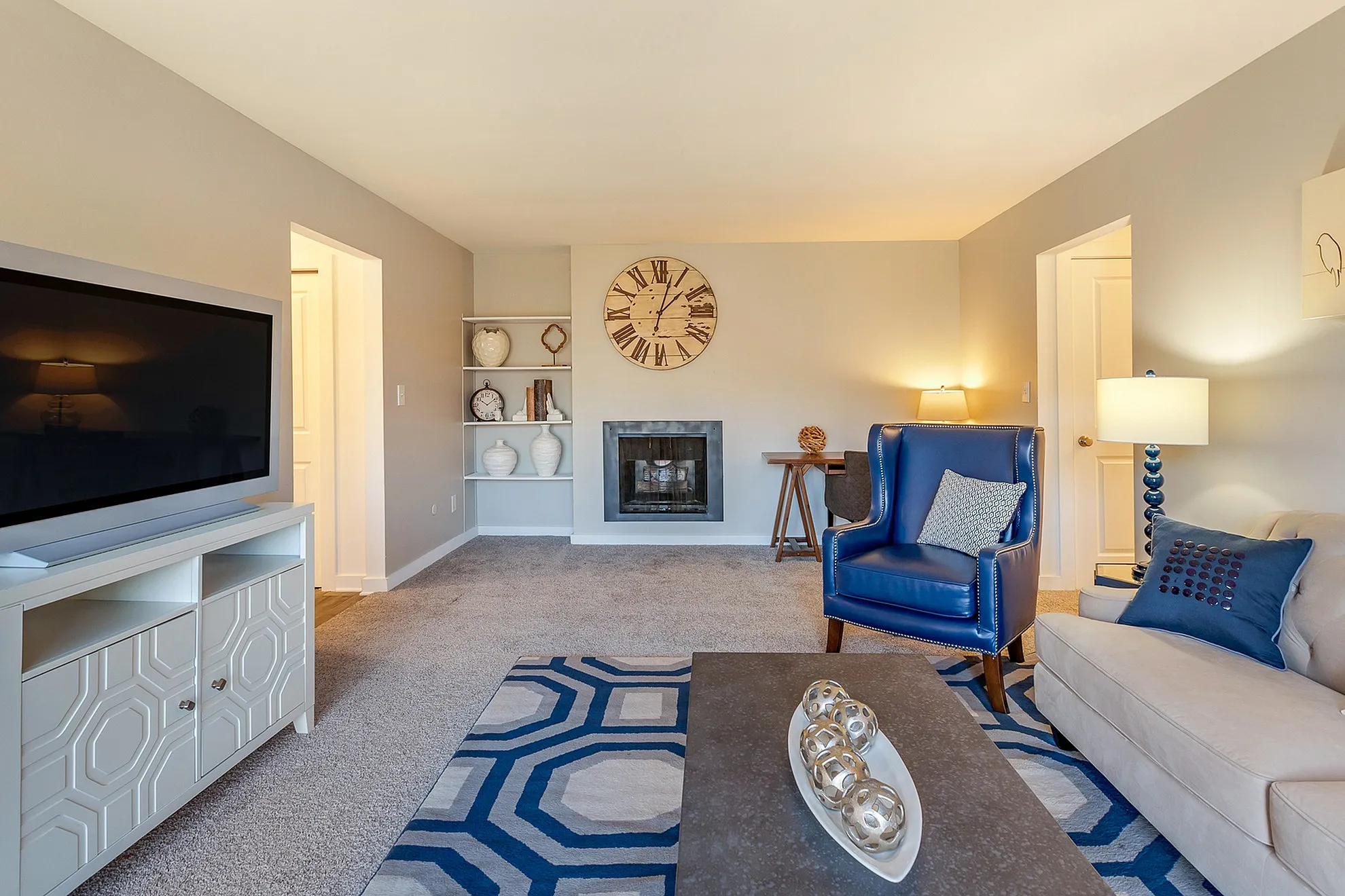 Inviting modern living room with elegant furnishings, featuring a cozy fireplace, stylish blue armchair, and a large wall clock accent.