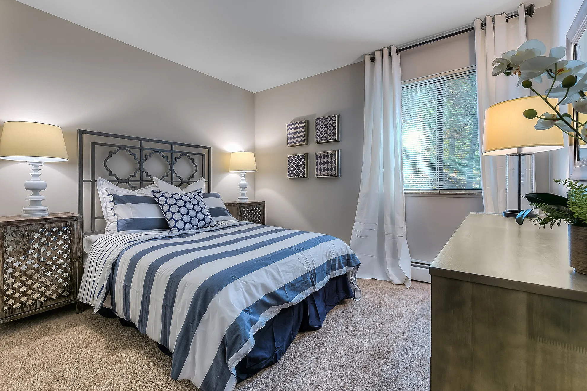 Cozy bedroom with elegant decor, featuring stylish striped bedding, ambient lighting, and large window enhancing natural light.