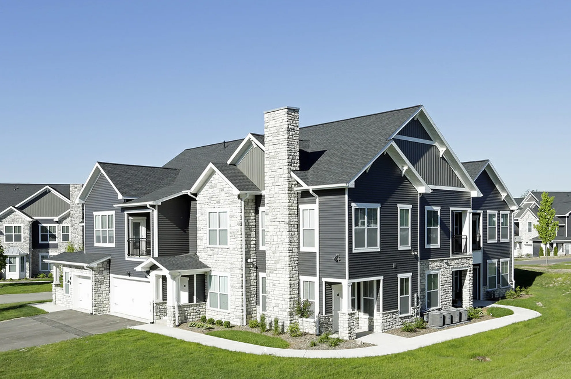 Charming modern duplex with stone accents, large windows, and lush green surroundings.