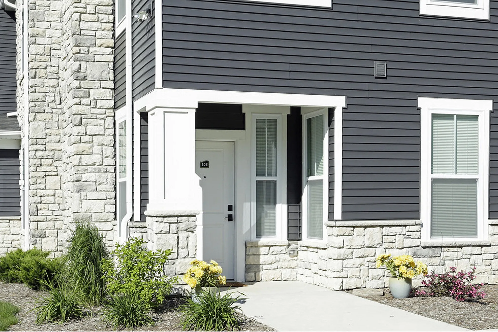 Inviting apartment entrance with modern stone accents and charming landscaping, highlighting a welcoming atmosphere.