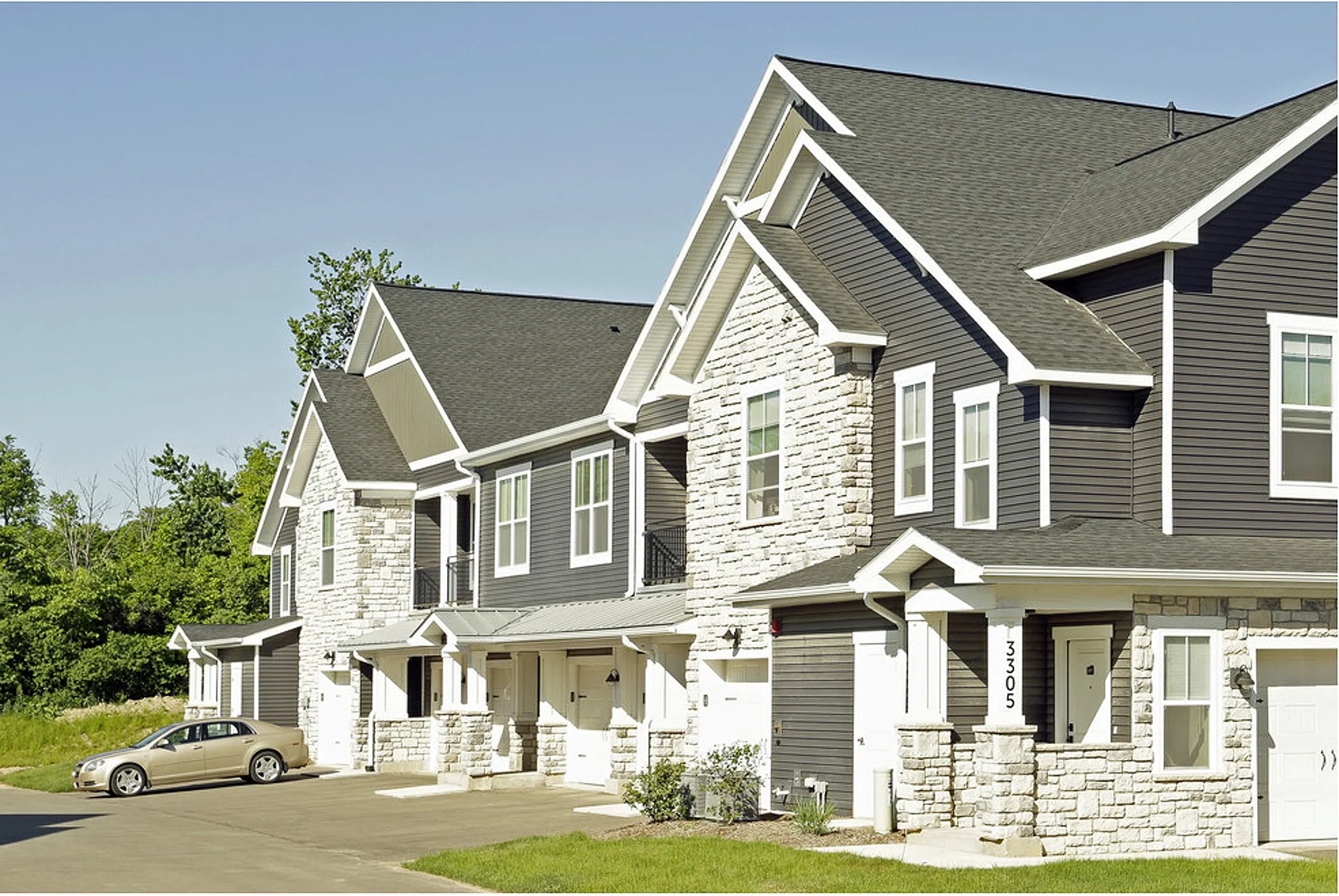 Charming townhouse with stone facade, modern siding, and welcoming driveway in a tranquil suburban setting.