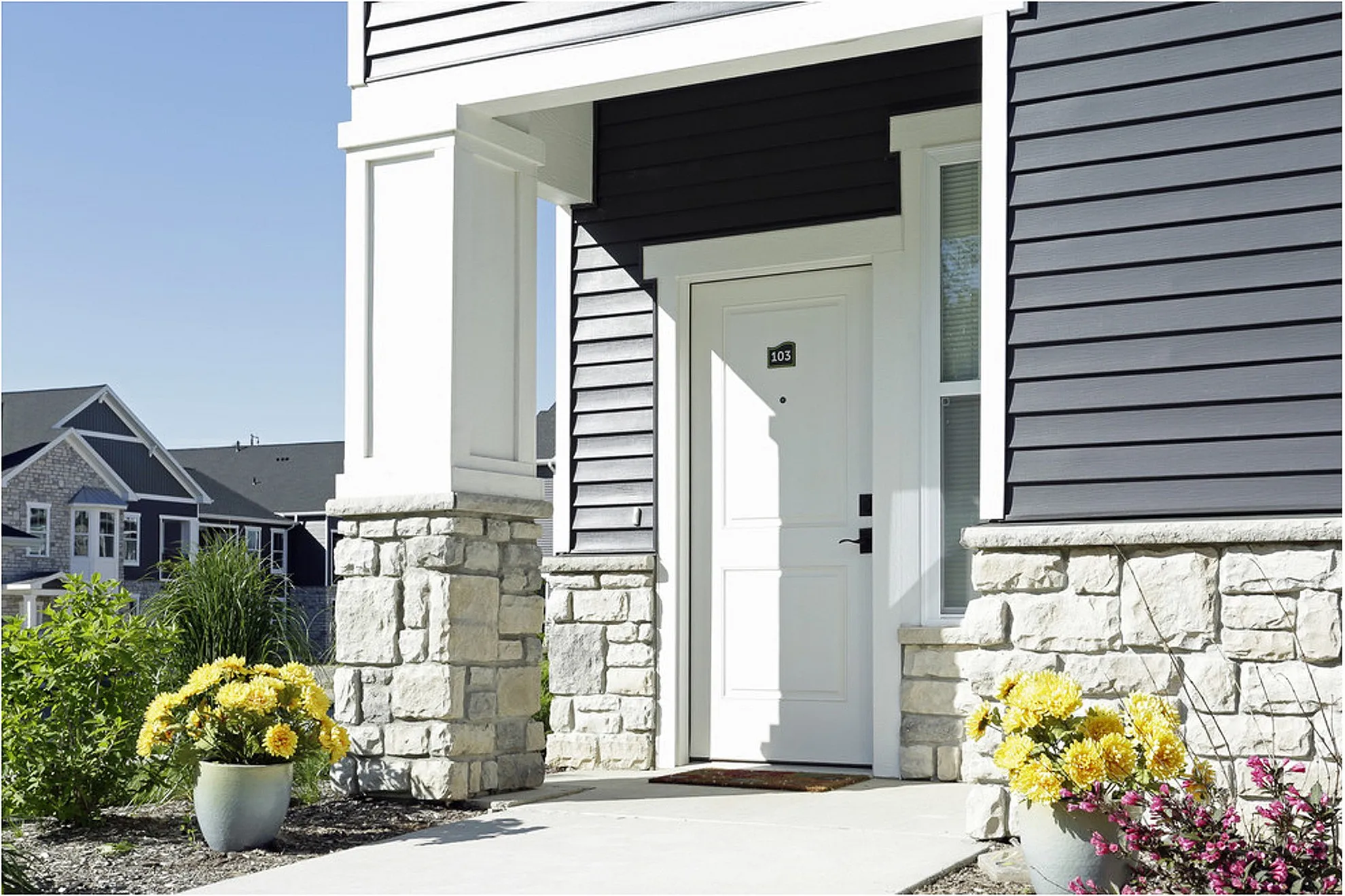 Charming front entrance of a modern apartment with elegant stone accents, vibrant flowers, and a welcoming atmosphere.