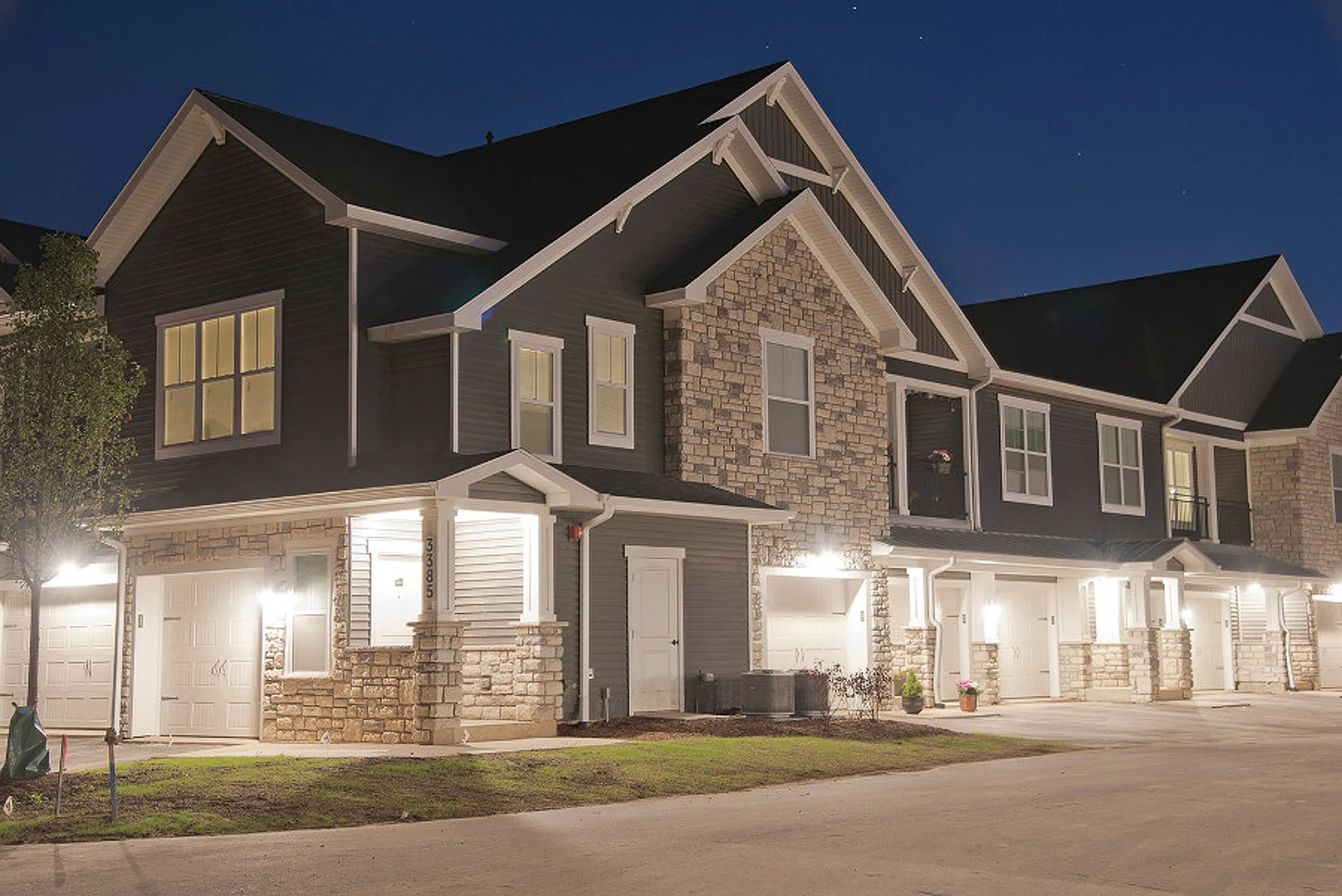 Charming townhouse exterior with elegant stonework and well-lit porch, set in a serene neighborhood evening scene.