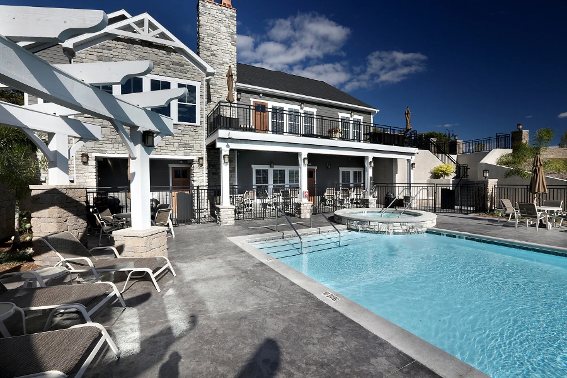 Luxurious outdoor pool area with jacuzzi and stylish loungers beside a modern apartment building with stone accents.