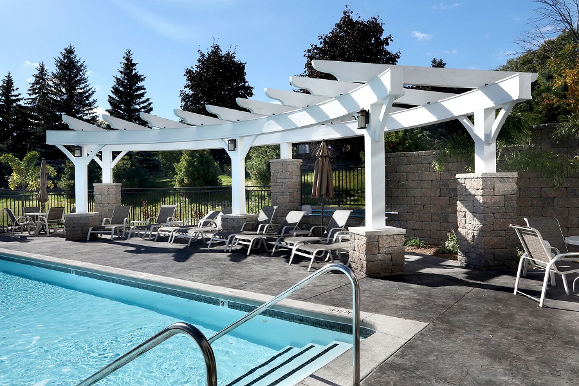 Inviting outdoor pool with elegant pergola and lounge chairs, surrounded by lush greenery for ultimate relaxation.