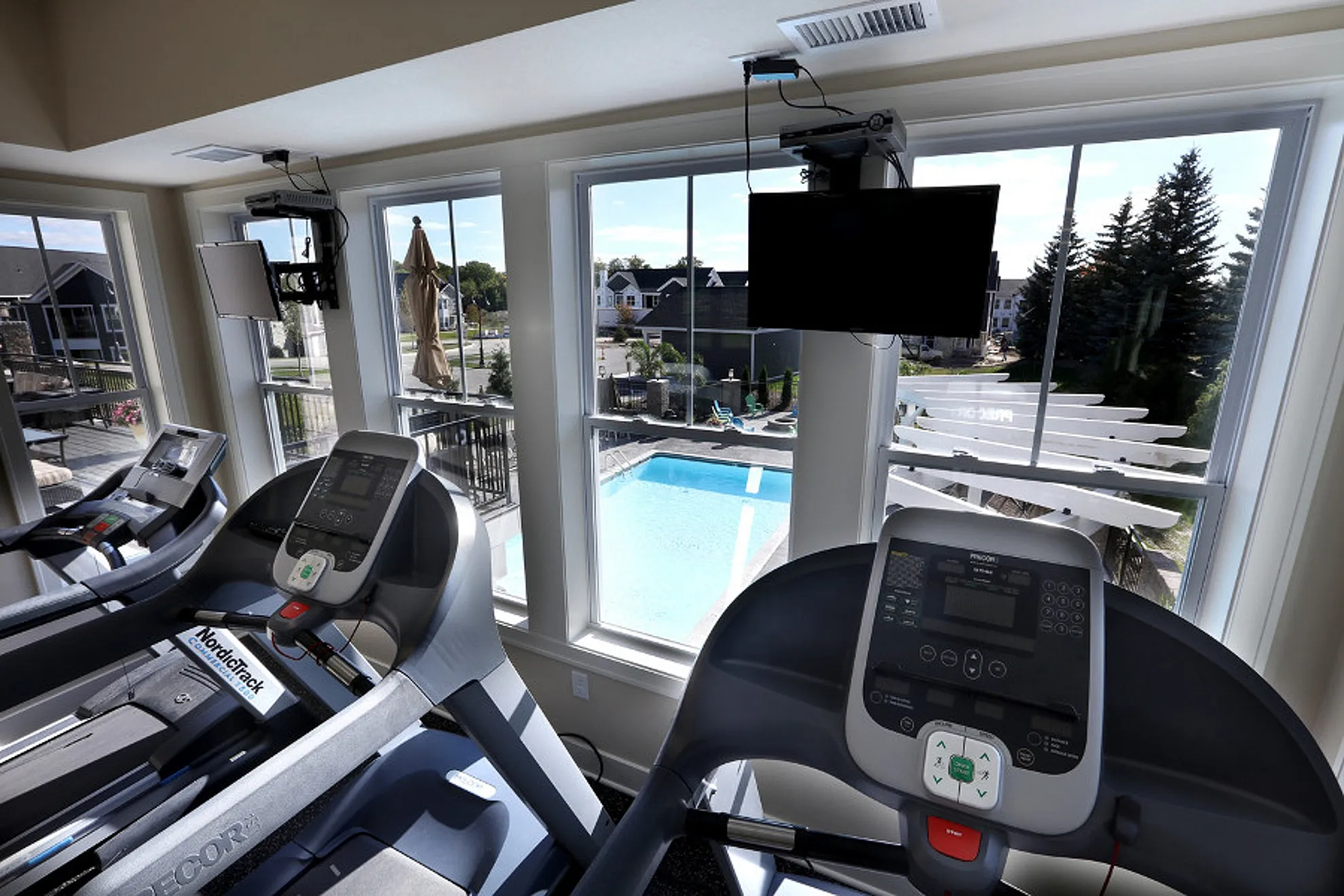 Modern fitness center with treadmills overlooking a luxurious outdoor pool and landscaped surroundings.