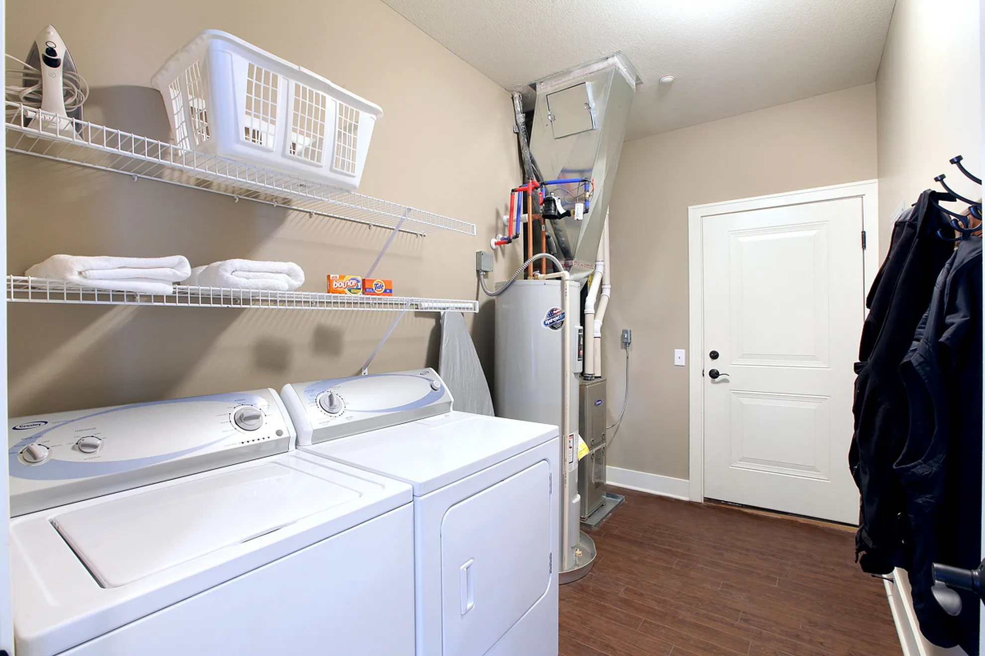 Modern laundry room featuring efficient washer and dryer, ample shelving, and sleek wooden flooring.