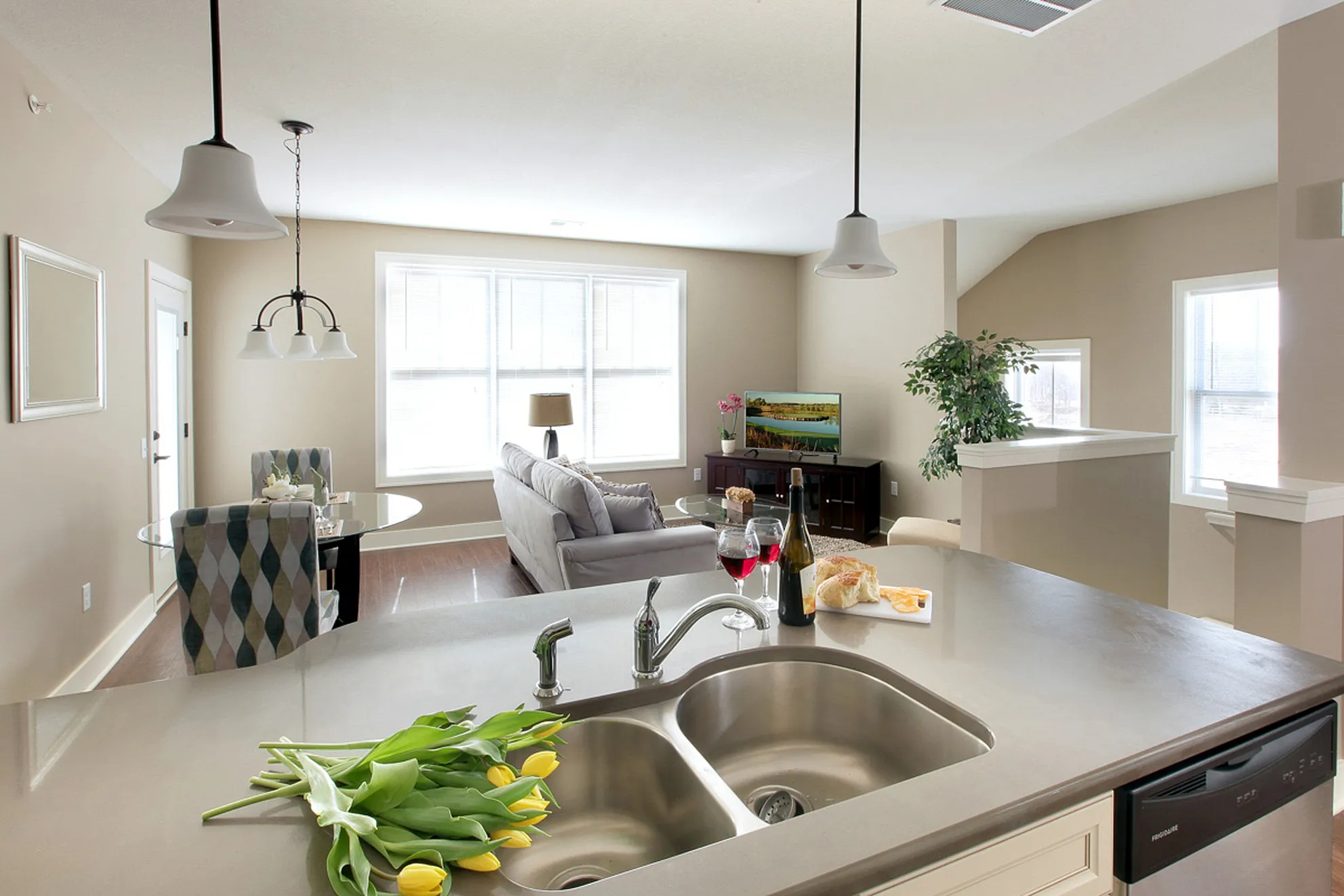 Modern open-concept living space featuring a sleek kitchen island with double sink, cozy dining area, and sunlit lounge with elegant decor.
