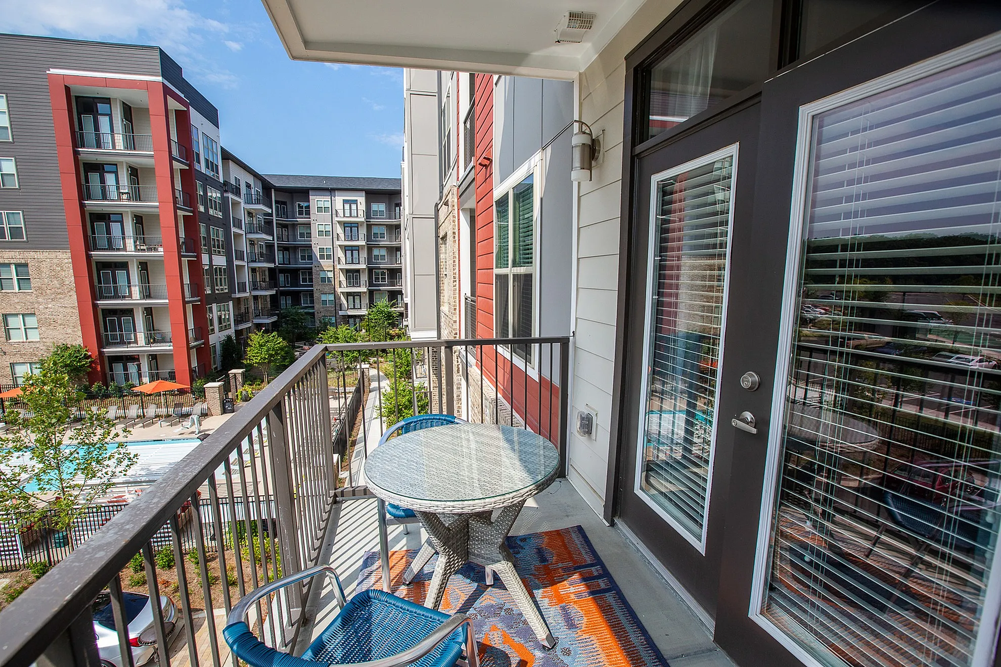 Charming balcony view of modern apartment complex with outdoor pool, colorful patio furniture, and elegant glass doors.