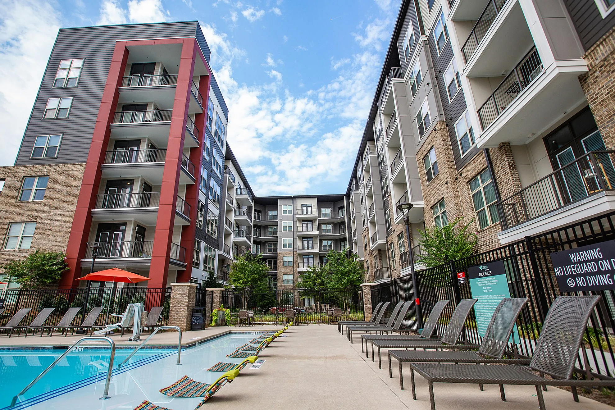 Modern apartment complex featuring stylish architecture, a refreshing pool, and sun loungers, perfect for relaxation and upscale living.