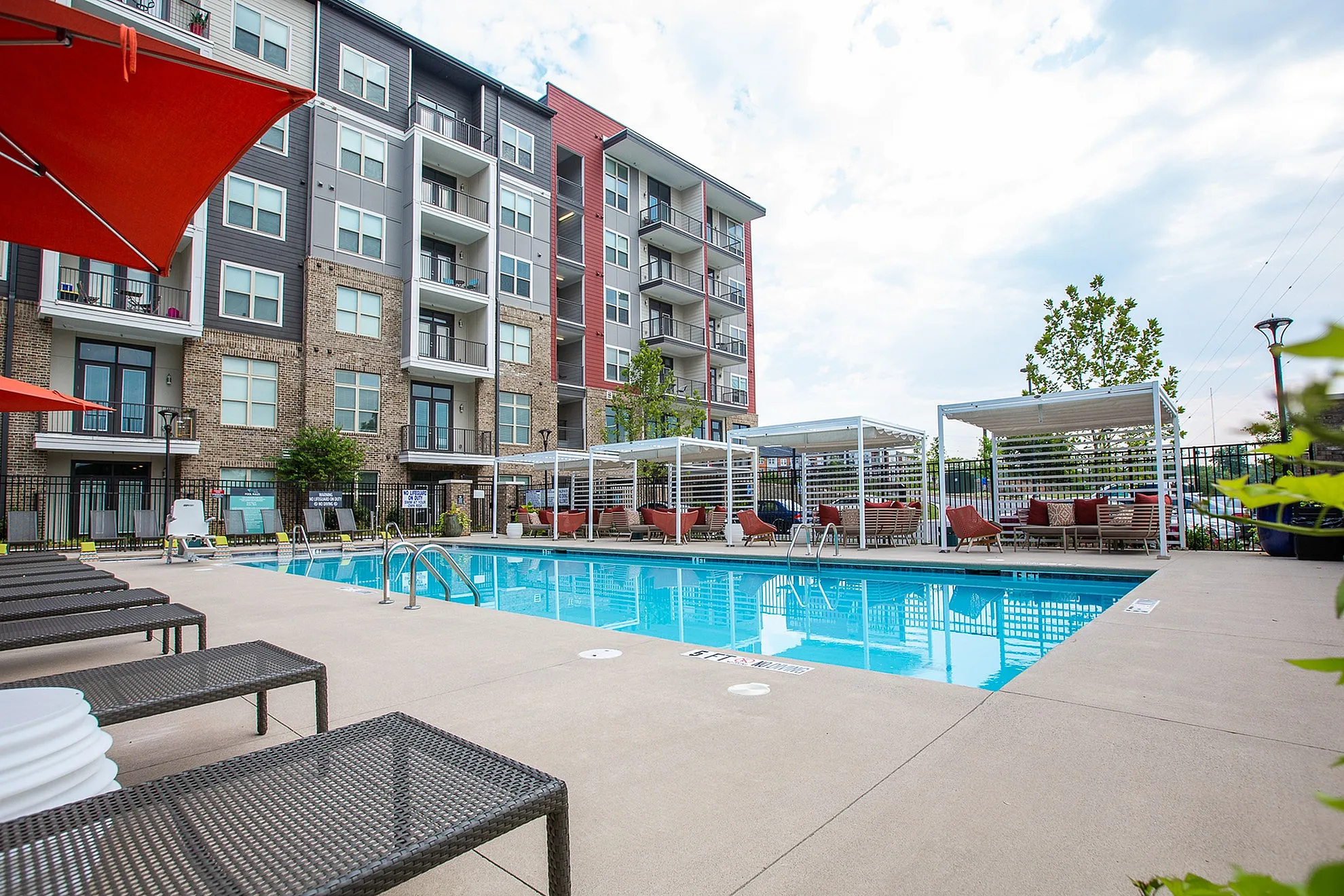 Modern apartment complex with a luxurious outdoor pool surrounded by cozy lounge chairs and private cabanas, perfect for relaxation and leisure.