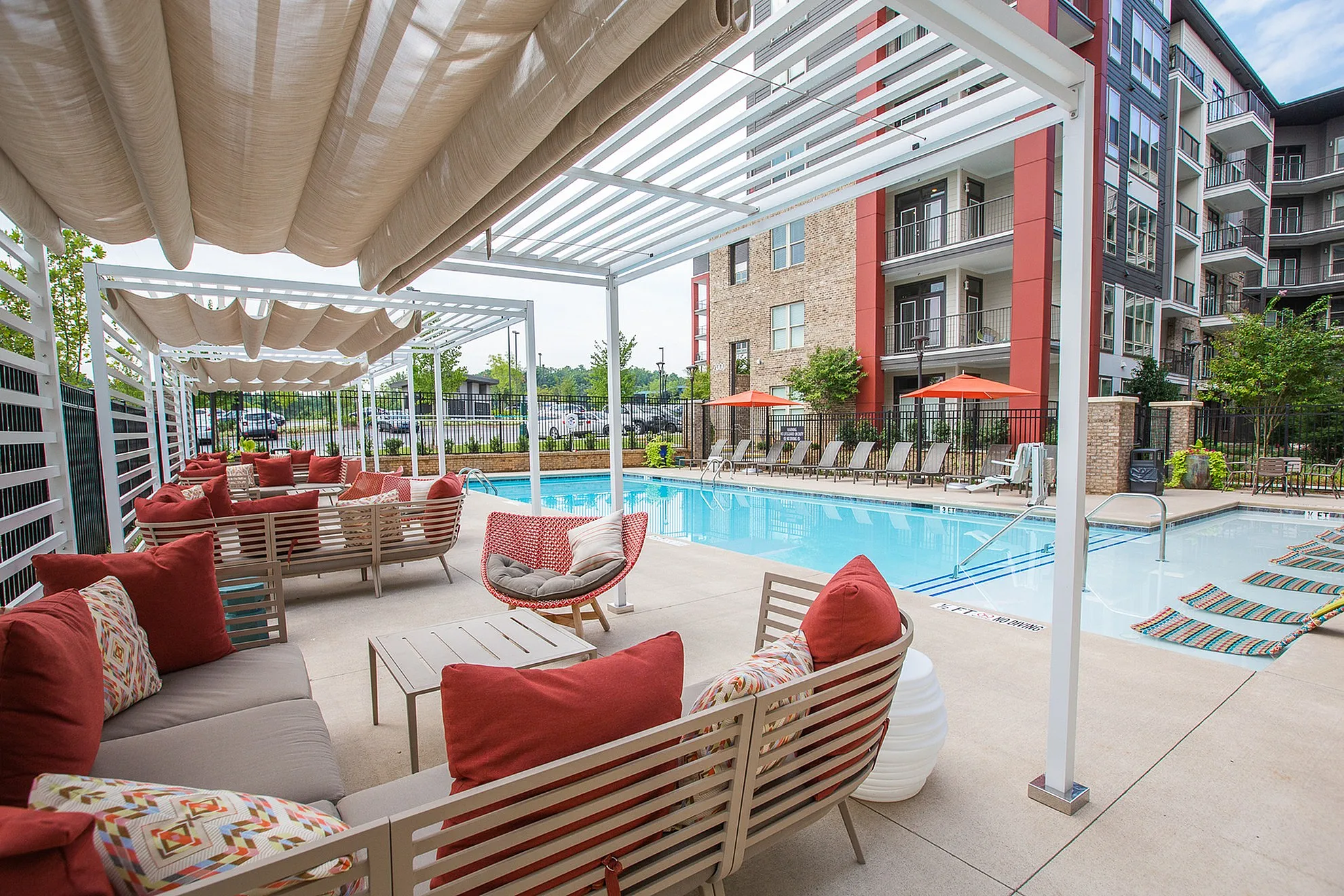 Inviting outdoor lounge area with cozy seating and vibrant pillows by a sparkling pool, perfect for relaxation and social gatherings.