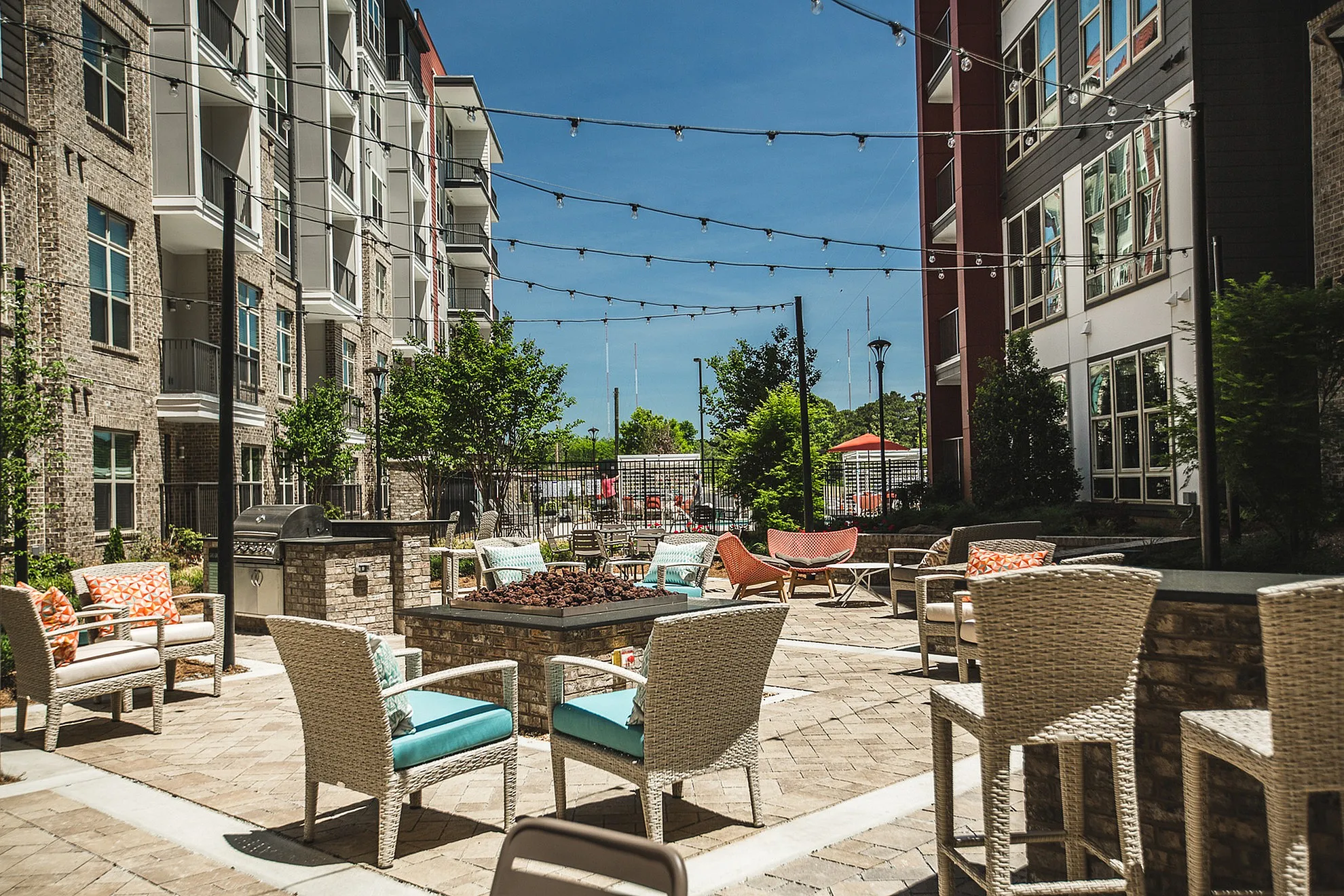 Inviting outdoor lounge area featuring modern wicker chairs, a cozy fire pit, and string lights in a stylish apartment complex courtyard.