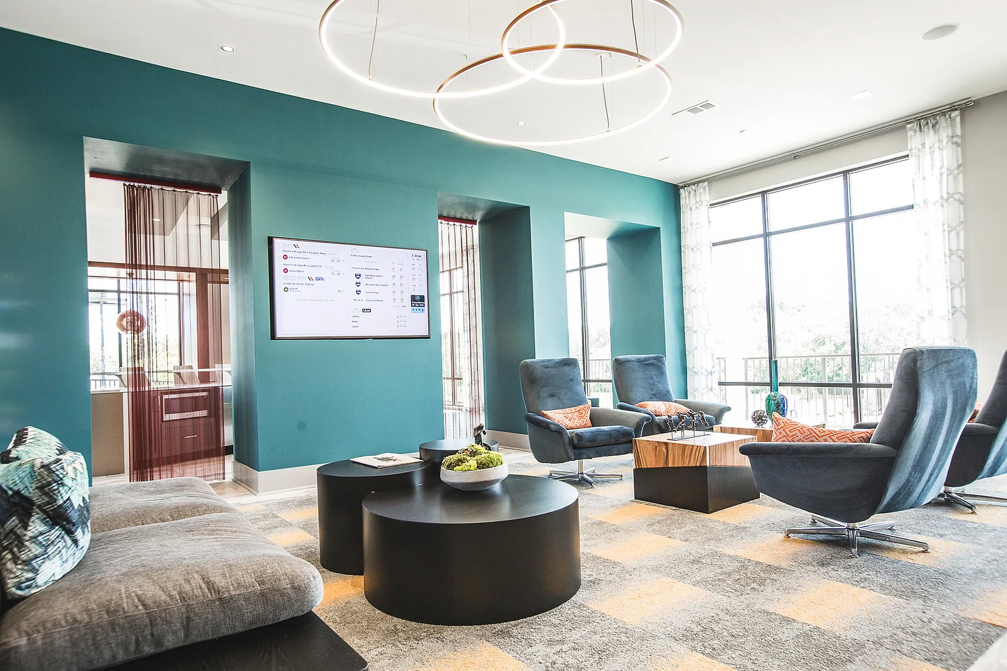 Modern lounge area with stylish seating, vibrant teal accent wall, and large windows offering natural light.