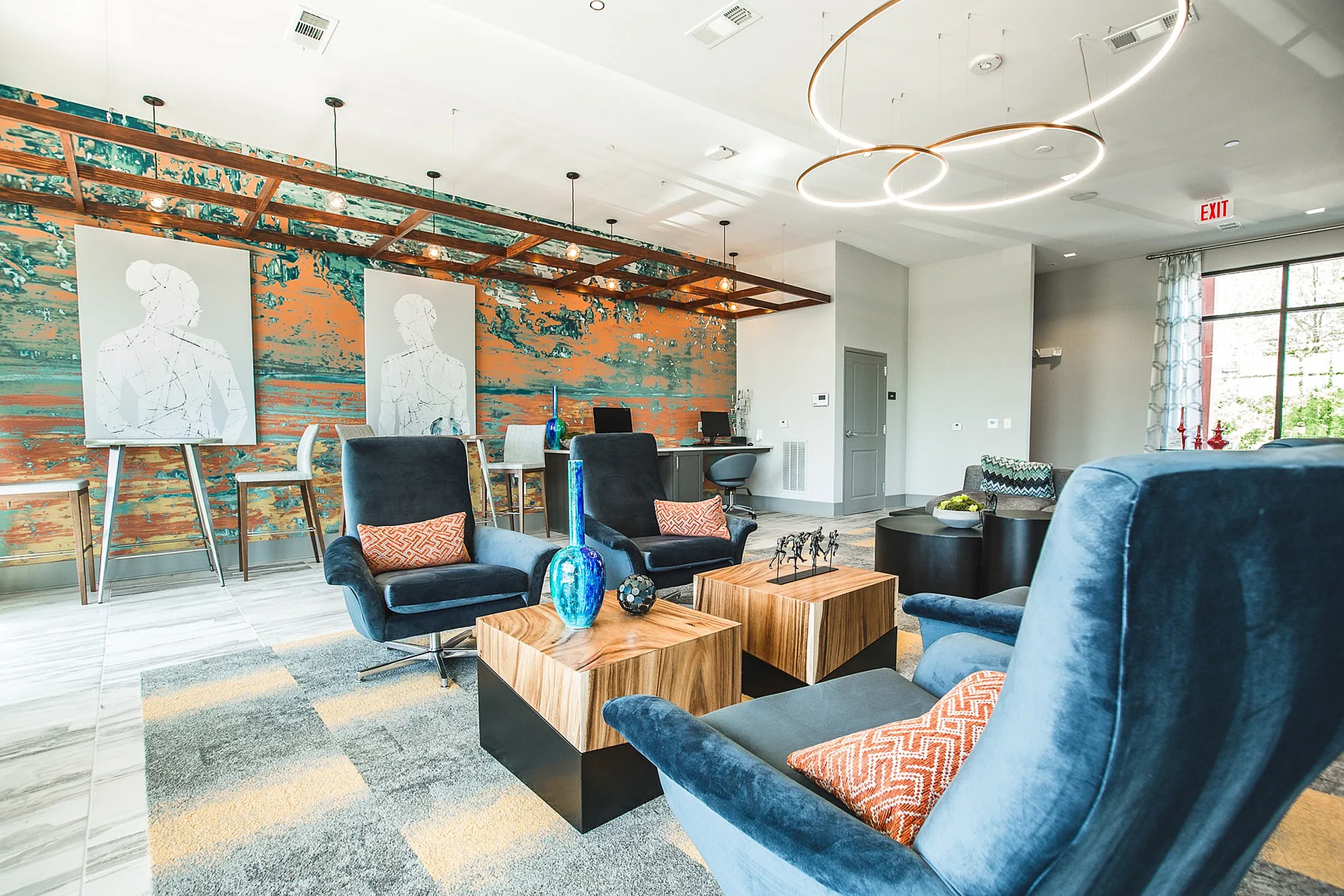 Modern lounge with stylish blue armchairs, vibrant abstract wall art, and chic wooden tables.