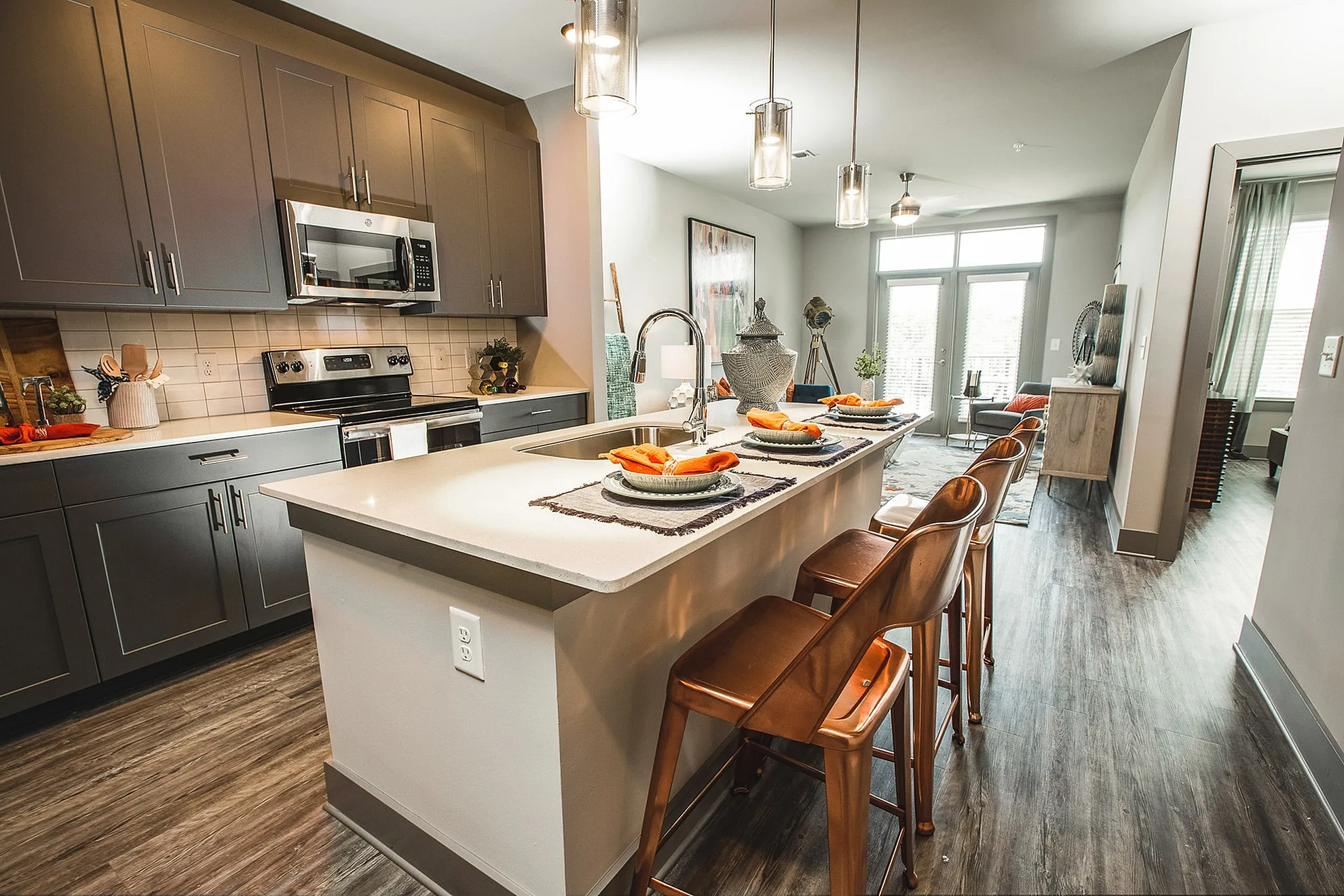 Modern apartment kitchen with sleek gray cabinetry, stylish island with bar seating, and inviting open-concept living area bathed in natural light.