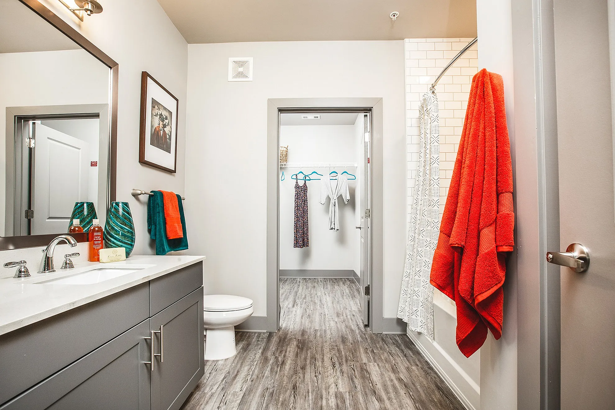 Modern bathroom featuring sleek countertops, vibrant red and teal towels, and a spacious walk-in closet, exuding comfort and style.
