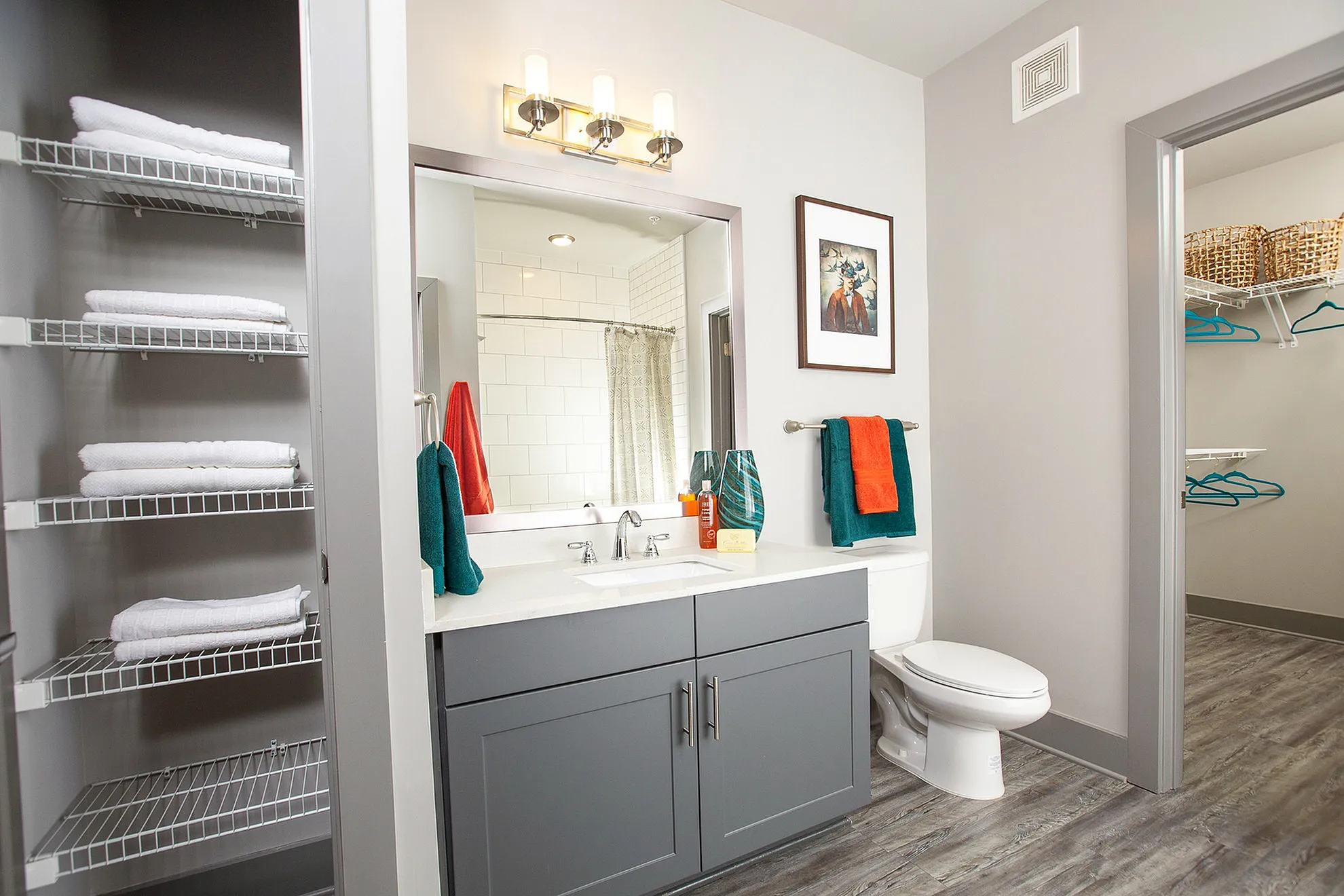 Chic bathroom with sleek gray vanity, modern lighting, and vibrant towel accents, adjacent to a spacious closet.