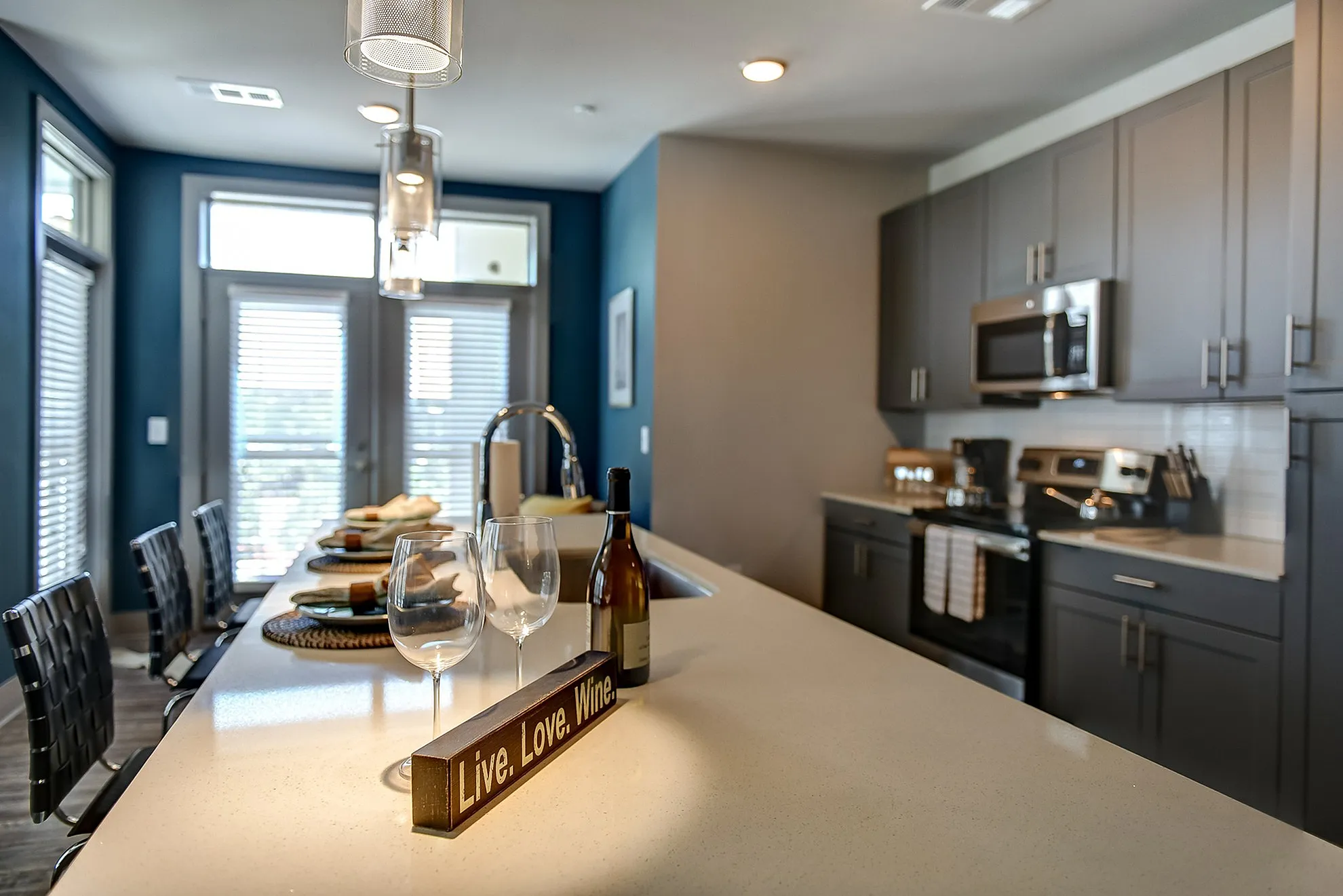 Modern kitchen with sleek gray cabinets, a polished countertop, and elegant pendant lighting. Includes stainless steel appliances and a cozy breakfast bar with chic decor.