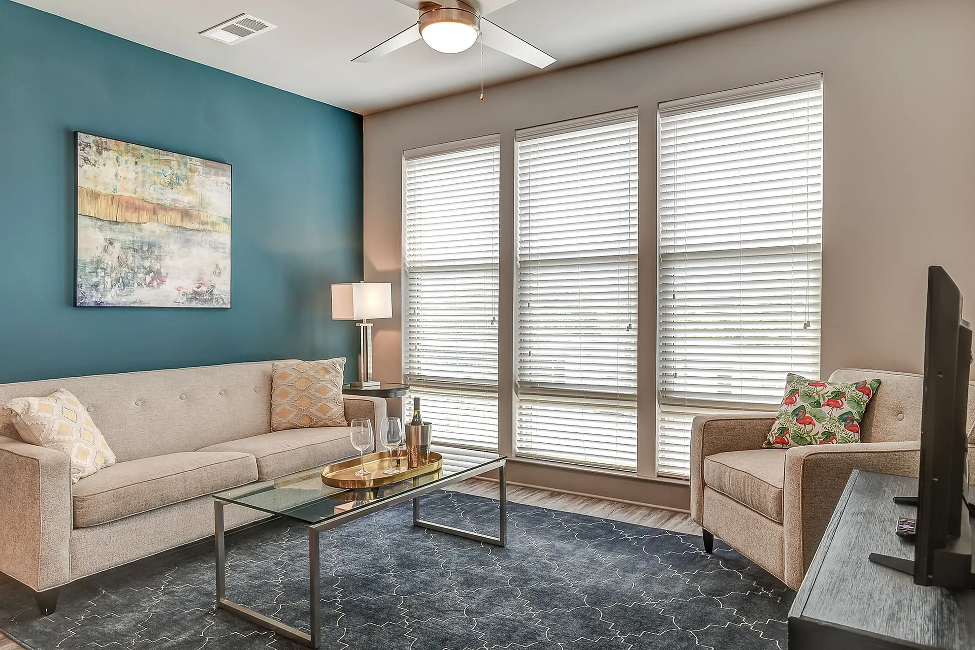 Inviting living room with elegant beige furniture, teal accent wall, and large sunlit windows, perfect for relaxation and entertaining.