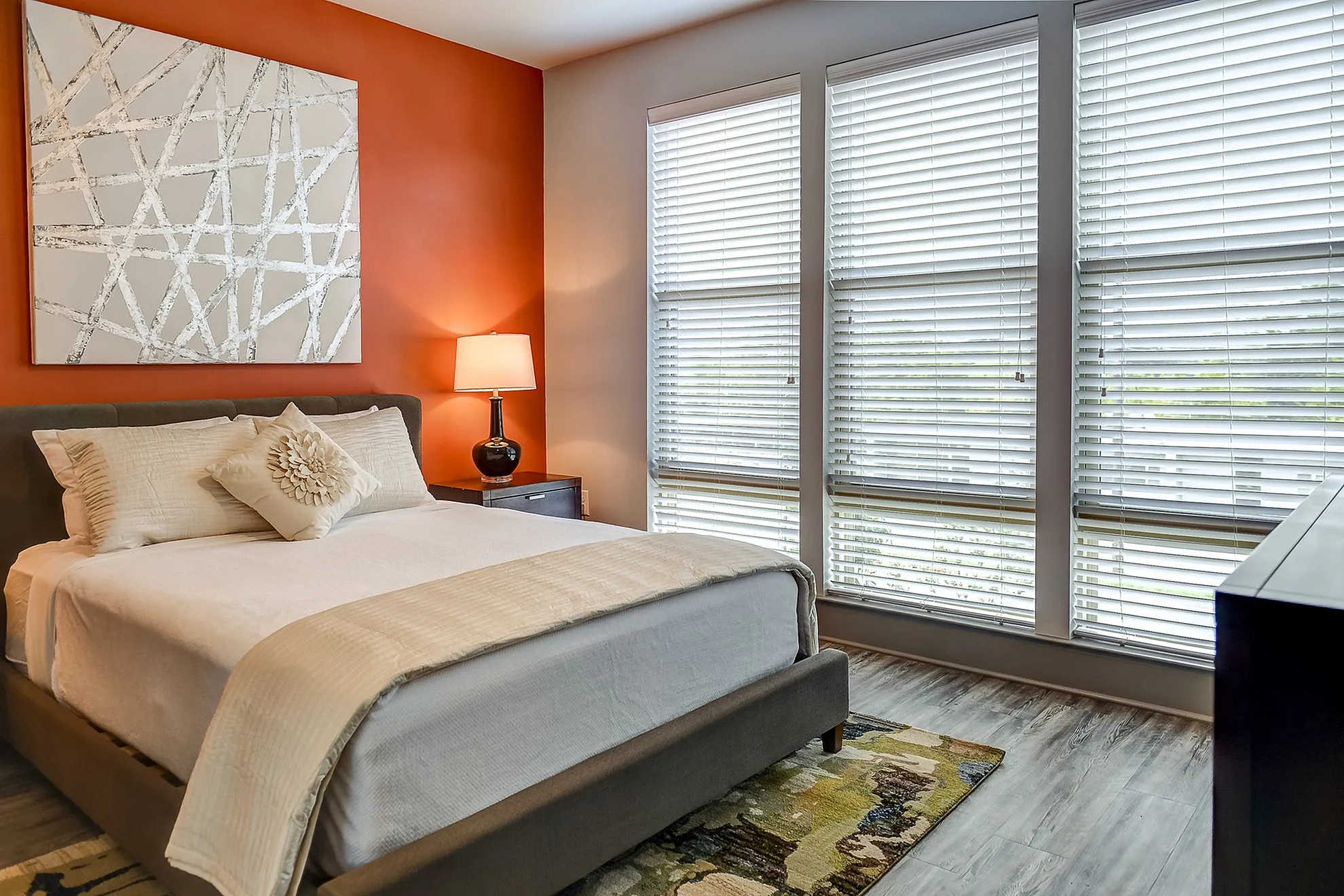 Inviting bedroom with a stylish orange accent wall, modern decor, and large windows for abundant natural light.