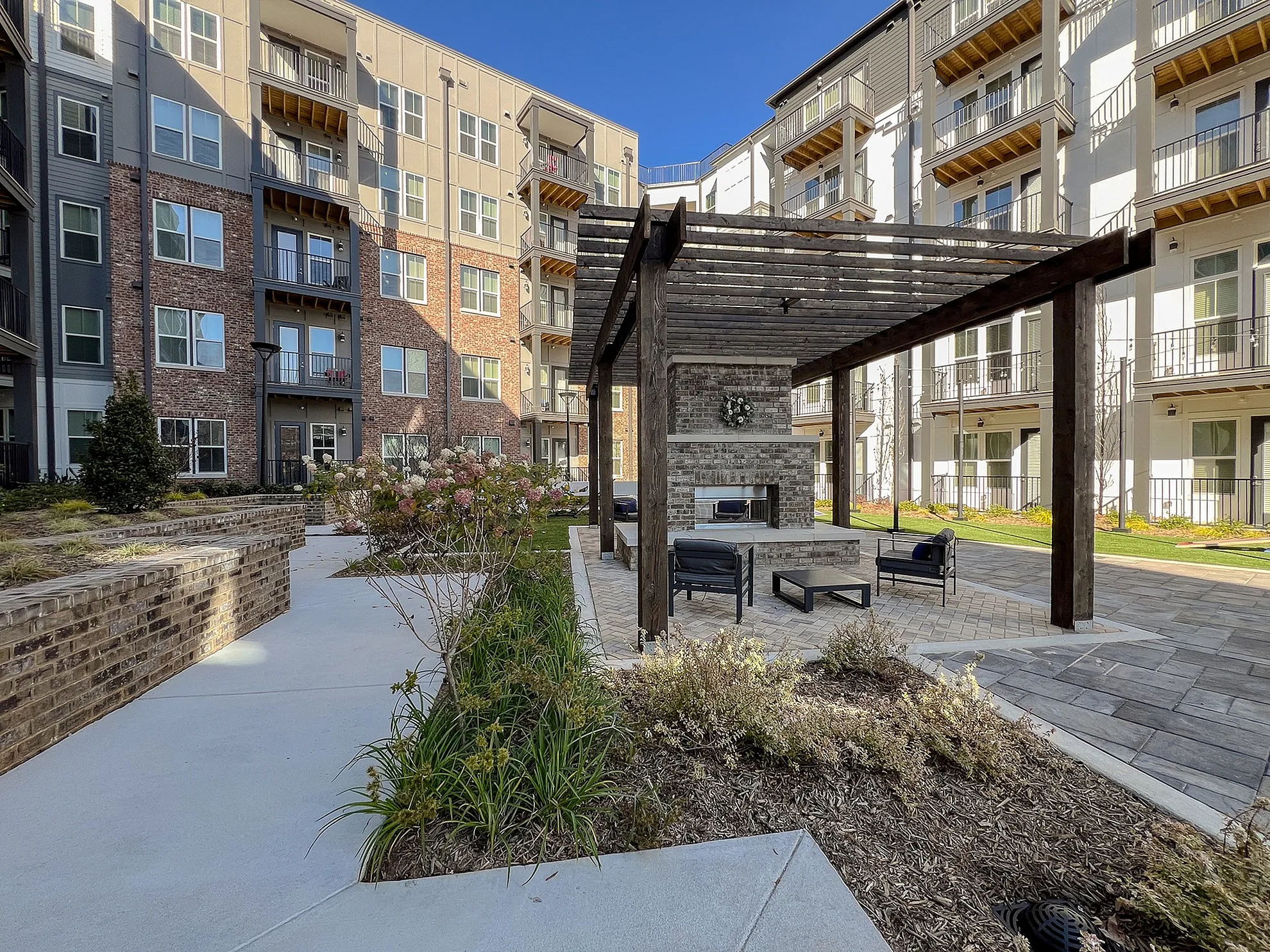 Charming apartment courtyard featuring a modern pergola with cozy seating, surrounded by lush landscaping and elegant multi-story buildings.