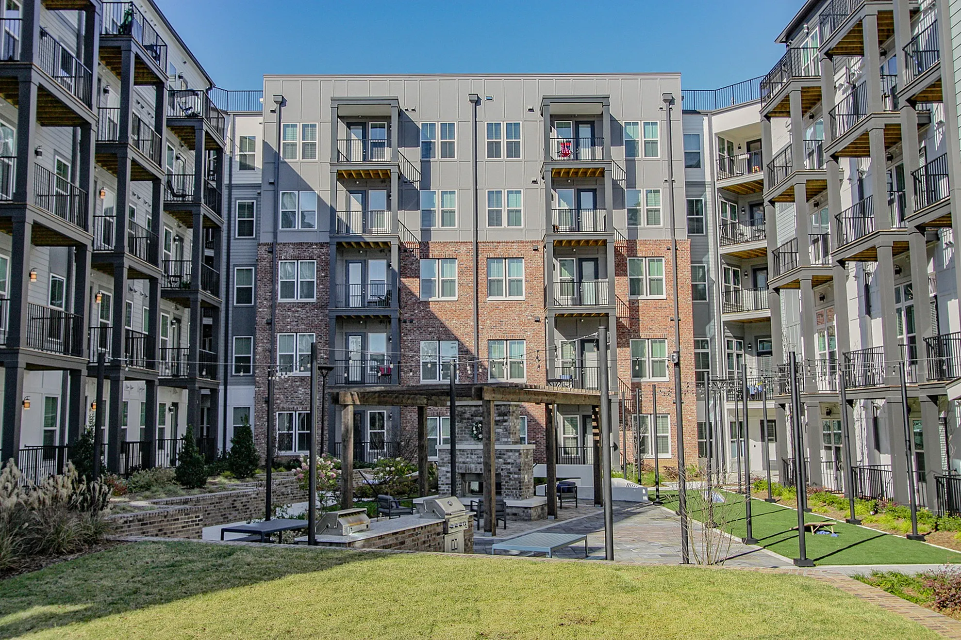 Modern apartment complex exterior with spacious balconies and a lush courtyard featuring seating and grilling areas for outdoor relaxation.