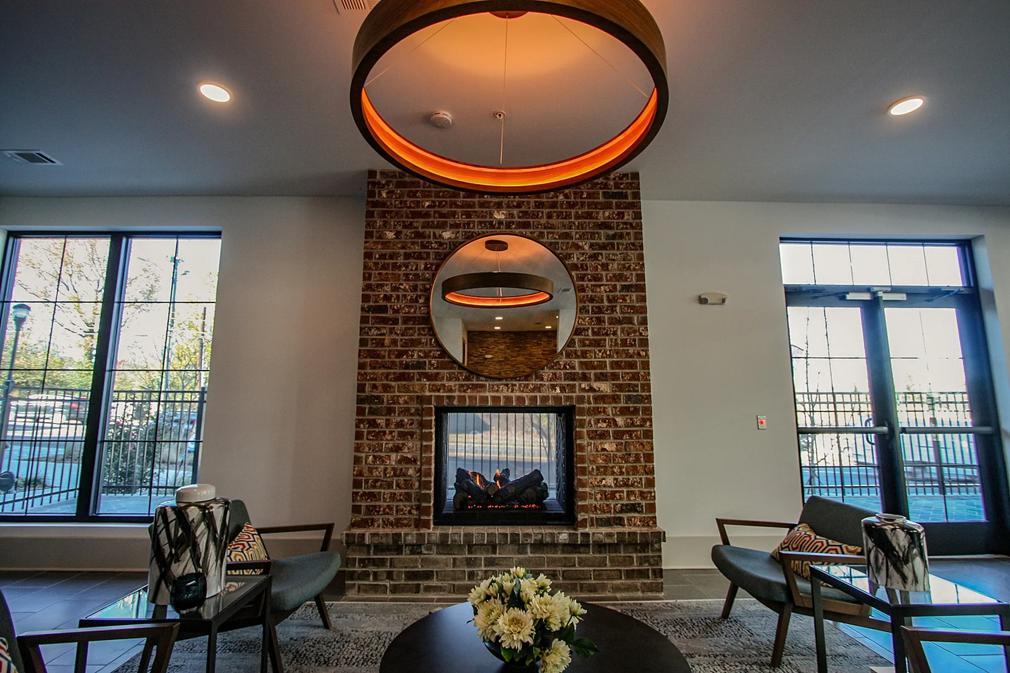 Modern lounge area featuring a stylish brick fireplace, elegant round mirror, and contemporary seating under warm lighting.